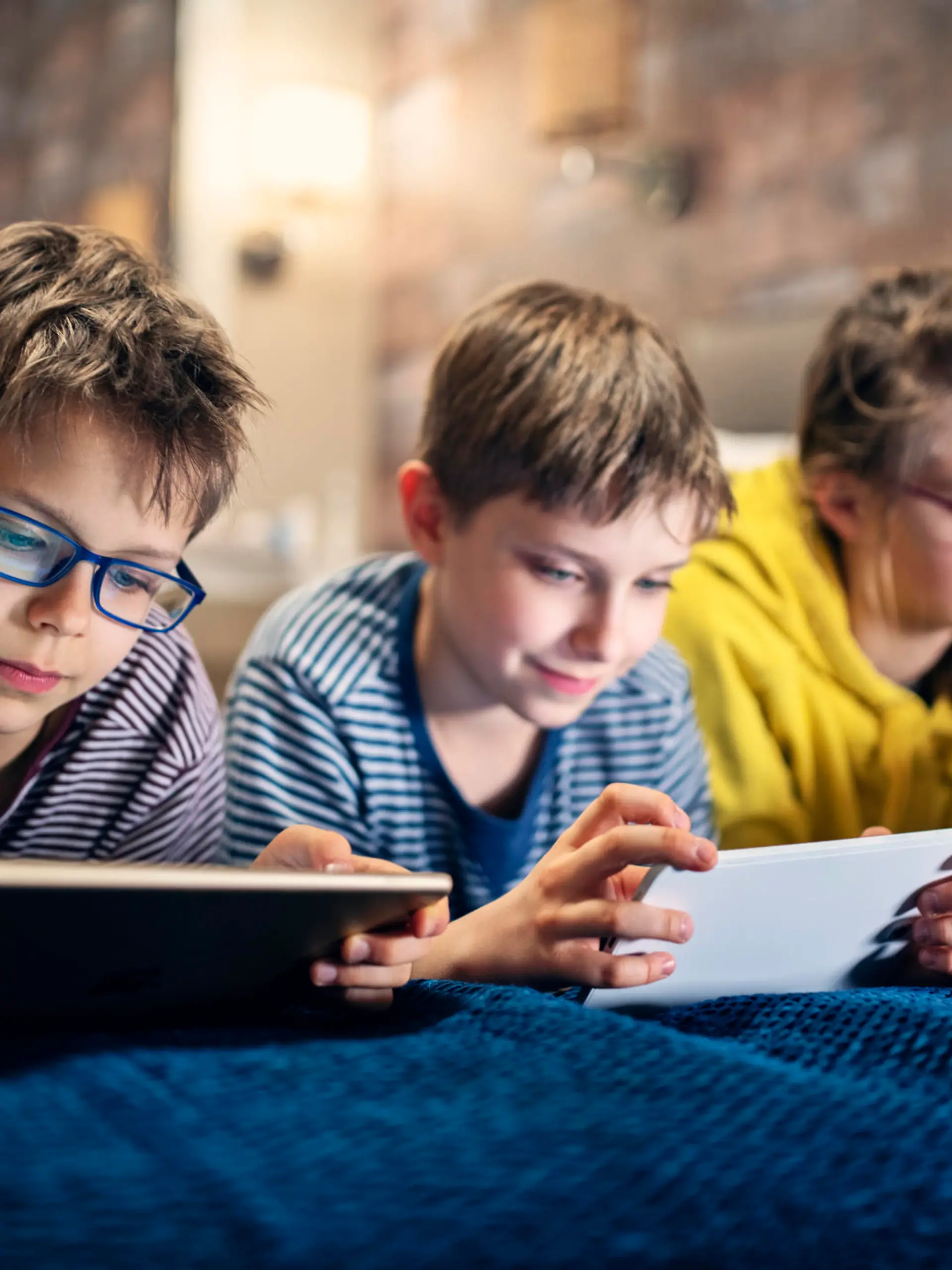 Three kids are lying on bed and playing with modern mobile devices - tablets and smartphone.
Nikon D850