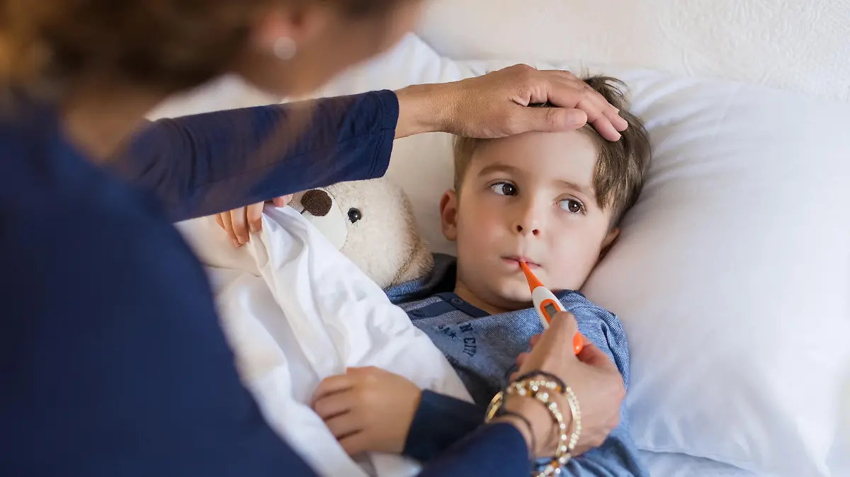 Sick boy with thermometer laying in bed and mother hand taking temperature. Mother checking temperature of her sick son who has thermometer in his mouth. Sick child with fever and illness while resting in bed.