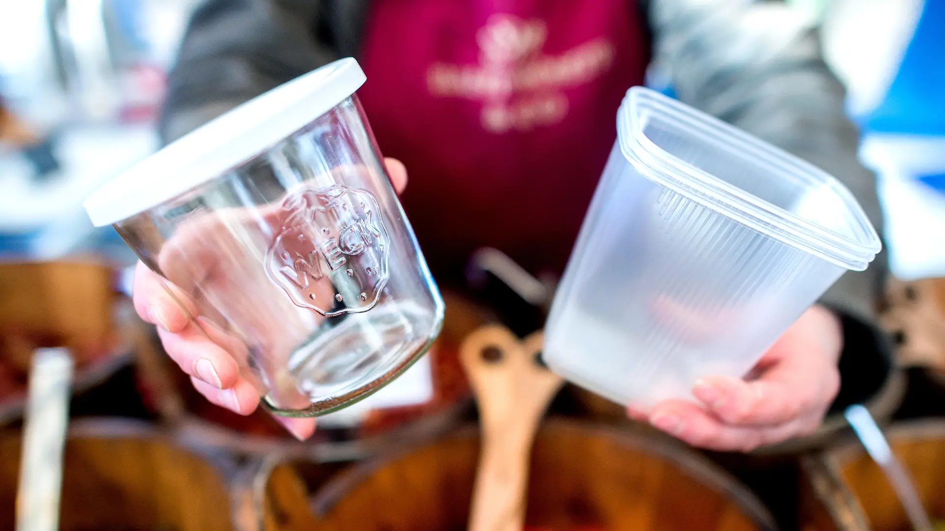 Eine Frau hält auf einem Wochenmarkt ein wiederverwendbares Glas und eine Einwegverpackung aus Plastik in den Händen. Mit dem wachsenden Umweltbewusstsein bei den Verbrauchern setzen die Verkäufer auf Wochenmärkten in Niedersachsen zunehmend auf nachhaltige Verpackungsalternativen.