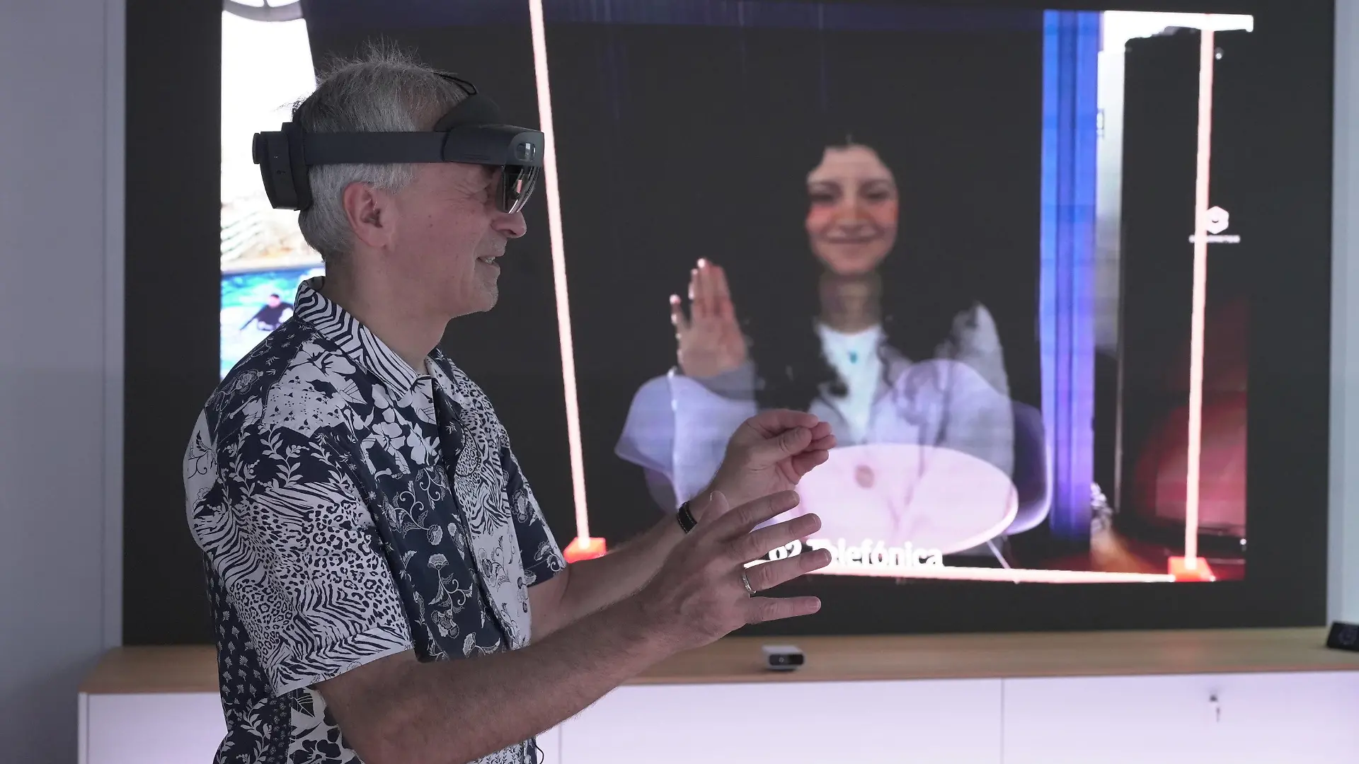 HANDOUT - 28.11.2023, Bayern, München: Karsten Erlebach, O2-Innovationsmanager, spricht via VR-Brille mit seiner Kollegin Fadia Abedrubh, die er in der Brille plastisch als Hologramm sieht. Auf dem Screen im Hintergrund spiegelt sich das wider - das Hintergrund-Bild wird nur zu Demo-Zwecken angezeigt. Der Mobilfunkanbieter Telefónica Deutschland (O2) will Hologramm-Telefonate, bei denen der Gesprächspartner als dreidimensionales Abbild zu sehen ist, im Jahr 2026 auf den Markt bringen. (zu dpa: «O2 will Hologramm-Telefonie ab 2026 anbieten») Foto: Barbaros Bulgurcu/o2 Telefonica/dpa - ACHTUNG: Nur zur redaktionellen Verwendung im Zusammenhang mit der aktuellen Berichterstattung und nur mit vollständiger Nennung des vorstehenden Credits +++ dpa-Bildfunk +++