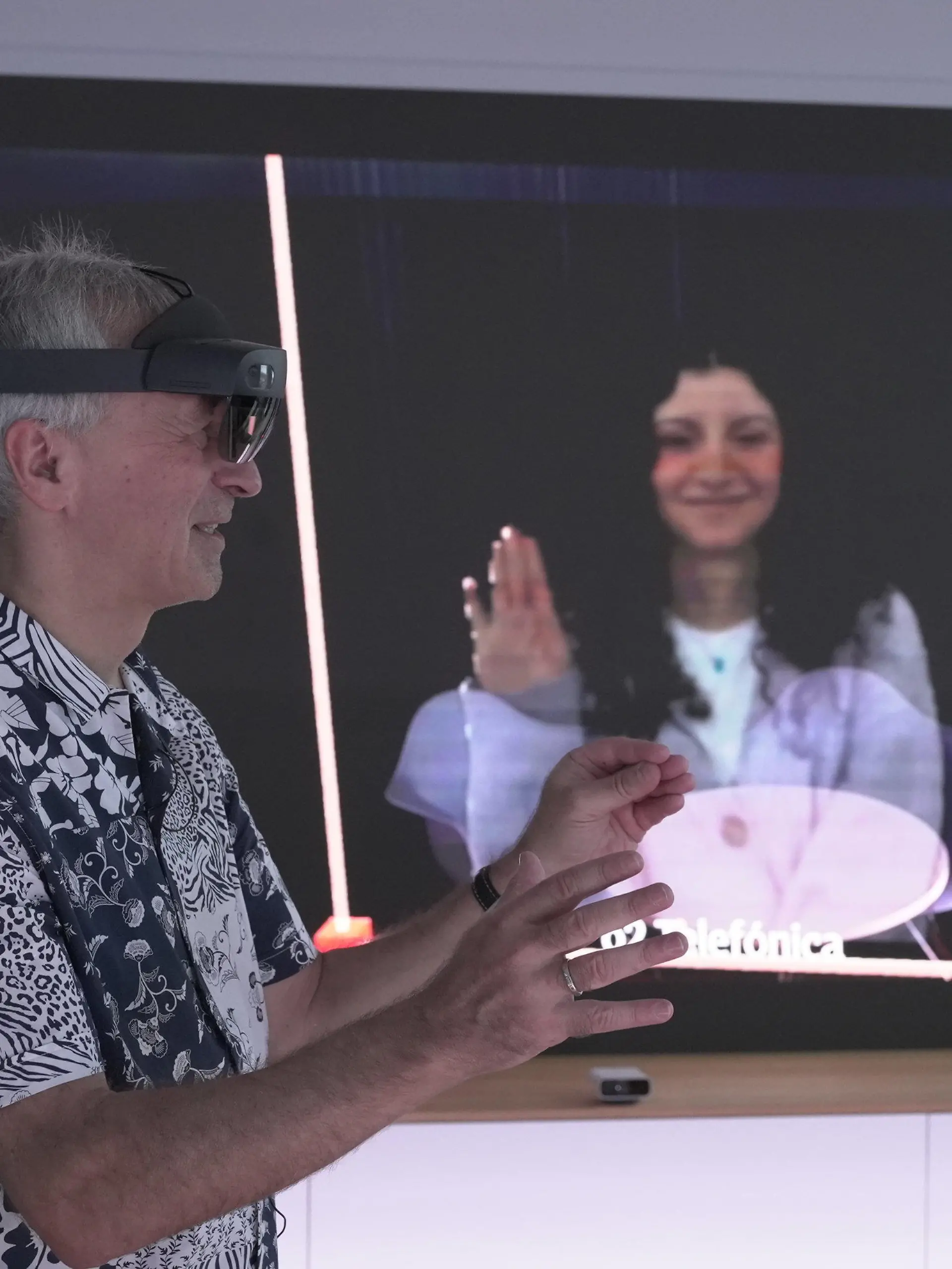 HANDOUT - 28.11.2023, Bayern, München: Karsten Erlebach, O2-Innovationsmanager, spricht via VR-Brille mit seiner Kollegin Fadia Abedrubh, die er in der Brille plastisch als Hologramm sieht. Auf dem Screen im Hintergrund spiegelt sich das wider - das Hintergrund-Bild wird nur zu Demo-Zwecken angezeigt. Der Mobilfunkanbieter Telefónica Deutschland (O2) will Hologramm-Telefonate, bei denen der Gesprächspartner als dreidimensionales Abbild zu sehen ist, im Jahr 2026 auf den Markt bringen. (zu dpa: «O2 will Hologramm-Telefonie ab 2026 anbieten») Foto: Barbaros Bulgurcu/o2 Telefonica/dpa - ACHTUNG: Nur zur redaktionellen Verwendung im Zusammenhang mit der aktuellen Berichterstattung und nur mit vollständiger Nennung des vorstehenden Credits +++ dpa-Bildfunk +++