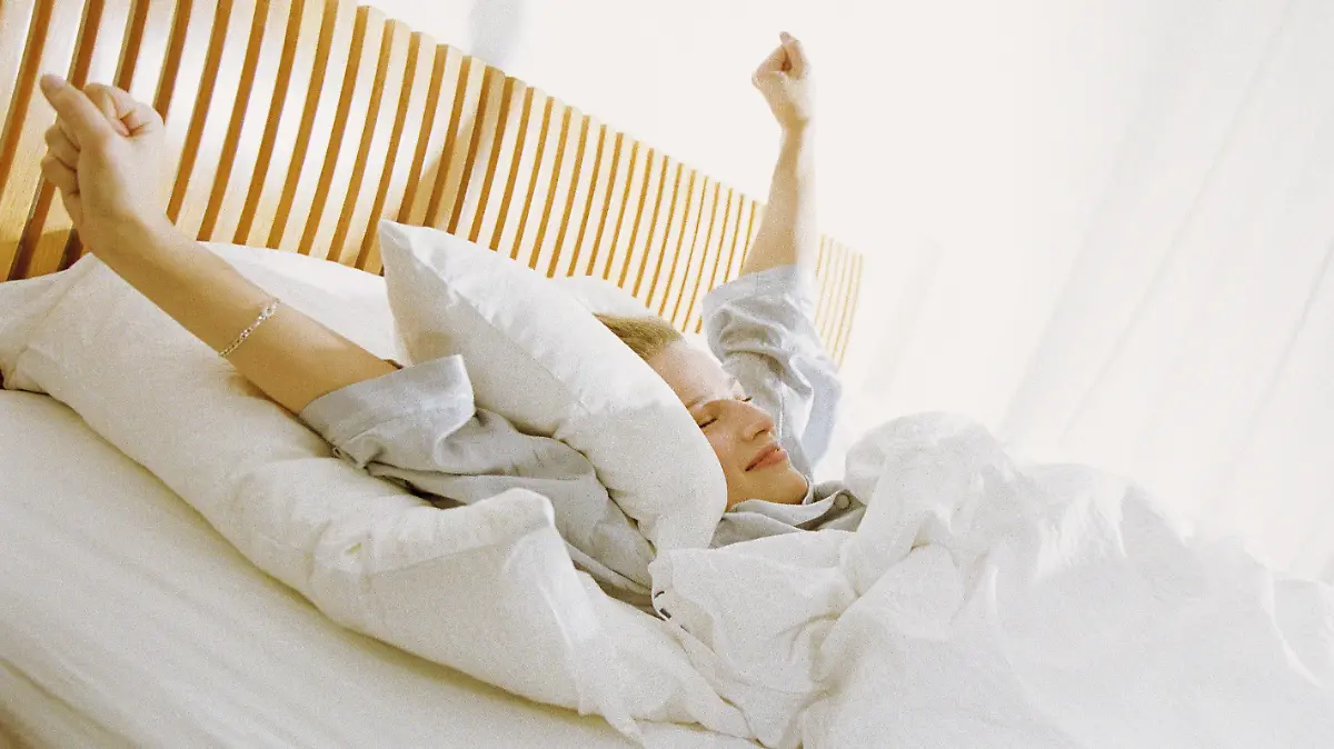 Eine Frau liegt im Bett und streckt sich.