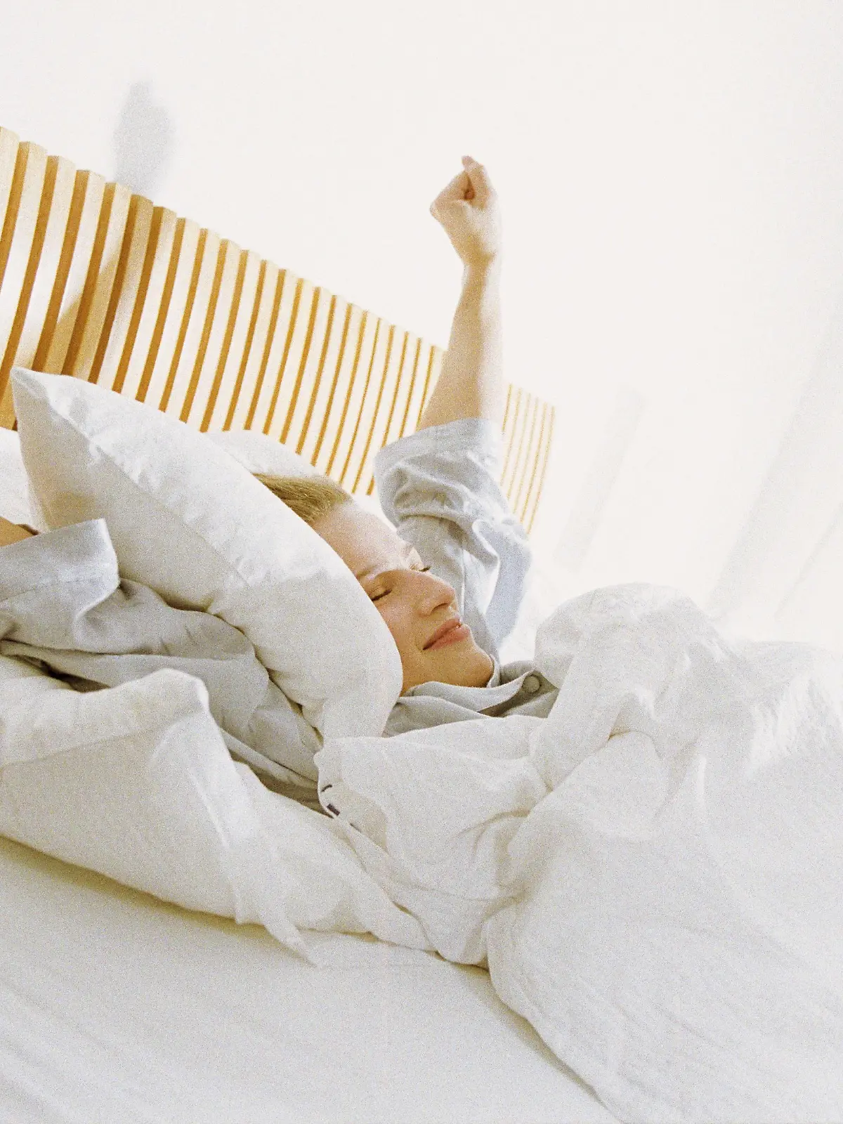 Eine Frau liegt im Bett und streckt sich.