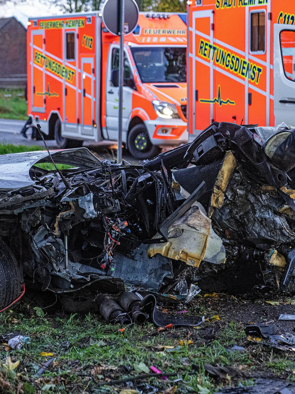 24.10.2022, Nordrhein-Westfalen, Rheurdt: Das Wrack eines Autos nach einem Unfall. Dahinter stehen Krankenwagen. Bei einem Aufprall eines Autos gegen einen Baum sind drei Menschen im Kreis Kleve ums Leben gekommen, darunter ein Kind und ein Säugling. Ein Mitfahrer habe lebensgefährliche Verletzungen erlitten, wie die Polizei am Montagabend mitteilte. Nach ersten Erkenntnissen der Ermittler war der Pkw aus unbekannter Ursache am Montagnachmittag bei Rheurdt-Schaephuysen von der Fahrbahn abgekommen und gegen den Baum geprallt. Foto: Arnulf Stoffel/dpa +++ dpa-Bildfunk +++