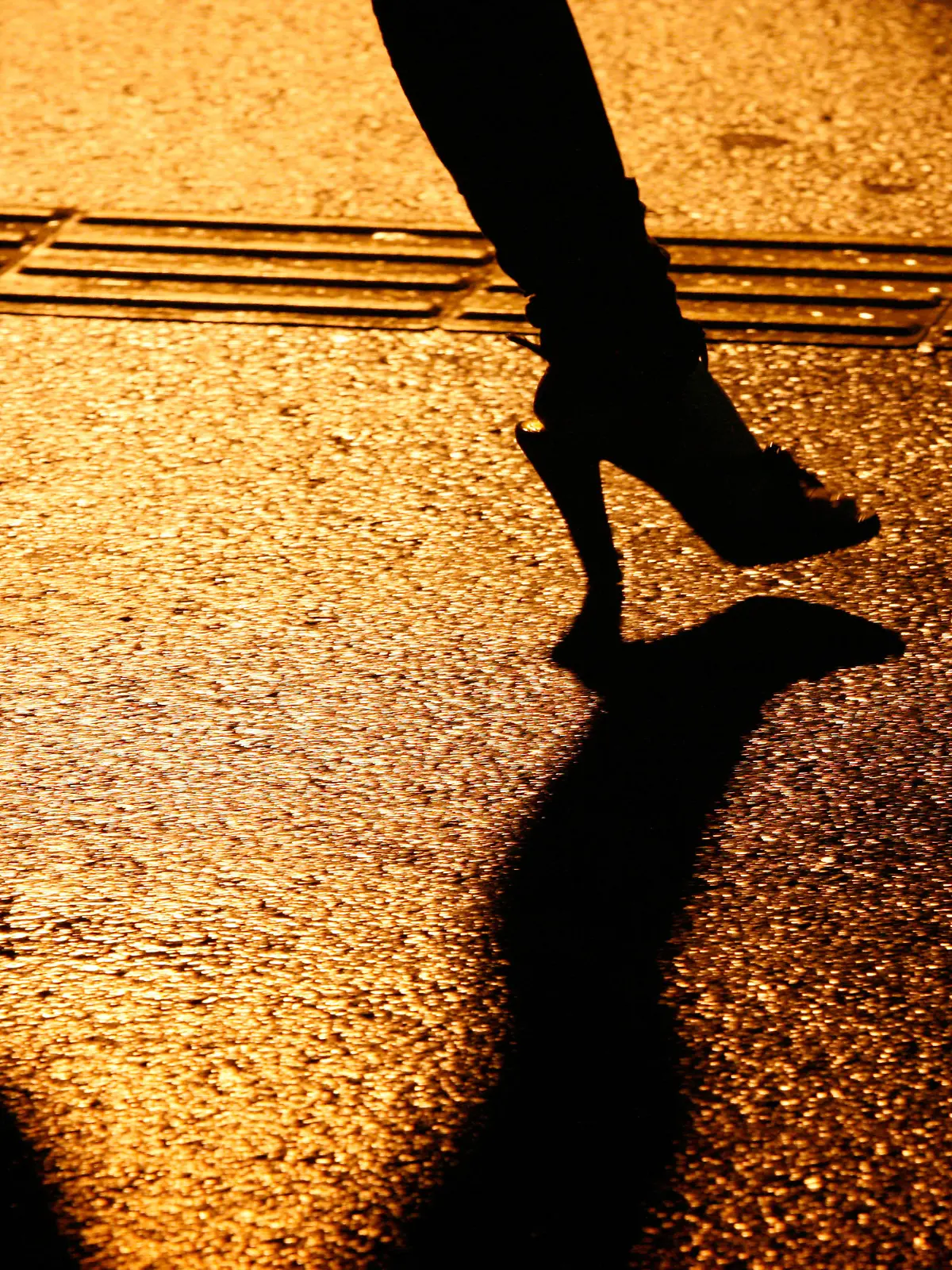 Junge Japanerin alleine auf einer regennassen Strasse in Shinjuku unterwegs, umgeben von dunklen Schatten hastet sie durch die Nacht. Shinjuku ist bekannt als Einkaufsmeile und Amuesierviertel mit Clubs, Bars, Restaurants, Karaoke, Shops und Rotlichtbezirk.
