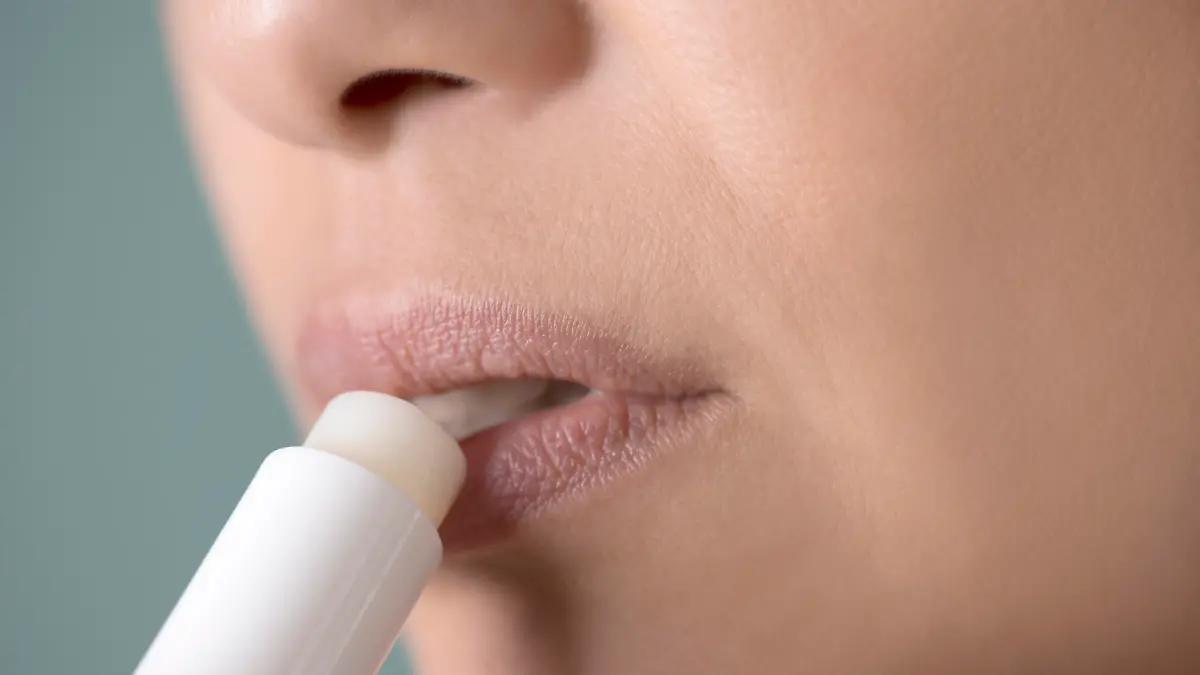 Caucasian female is using lip balm for her lips.