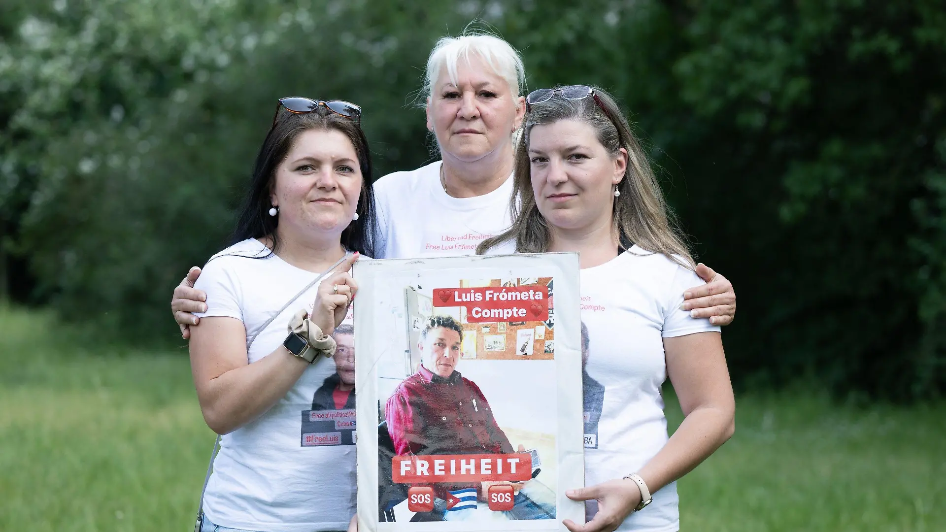 ARCHIV - 11.06.2023, Sachsen, Dresden: Maria (l) und Janie (r) Frometa Compte, Töchter des inhaftierten Deutsch-Kubaners Luis Frometa Compte, und Silke Frometa Compte, Ehefrau, stehen am Rande einer Kundgebung im Alaunpark und halten ein Foto von Luis Frometa Compte. Die Angehörigen eines in Kuba inhaftierten Deutschen sorgen sich um seinen Zustand, nachdem er im Gefängnis offenbar geschlagen und schwer verletzt wurde. (zu dpa «Familie: Deutscher im Knast in Kuba schwer verletzt - Besuch verwehrt») Foto: Sebastian Kahnert/dpa +++ dpa-Bildfunk +++