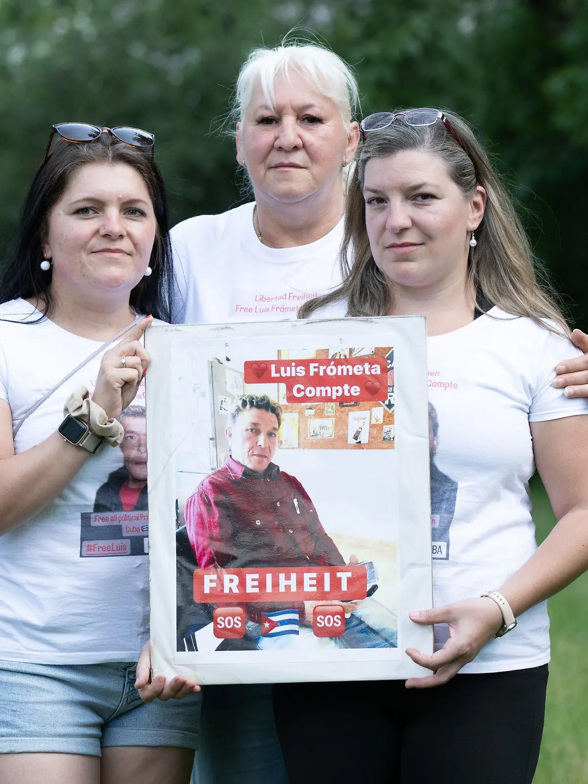 ARCHIV - 11.06.2023, Sachsen, Dresden: Maria (l) und Janie (r) Frometa Compte, Töchter des inhaftierten Deutsch-Kubaners Luis Frometa Compte, und Silke Frometa Compte, Ehefrau, stehen am Rande einer Kundgebung im Alaunpark und halten ein Foto von Luis Frometa Compte. Die Angehörigen eines in Kuba inhaftierten Deutschen sorgen sich um seinen Zustand, nachdem er im Gefängnis offenbar geschlagen und schwer verletzt wurde. (zu dpa «Familie: Deutscher im Knast in Kuba schwer verletzt - Besuch verwehrt») Foto: Sebastian Kahnert/dpa +++ dpa-Bildfunk +++