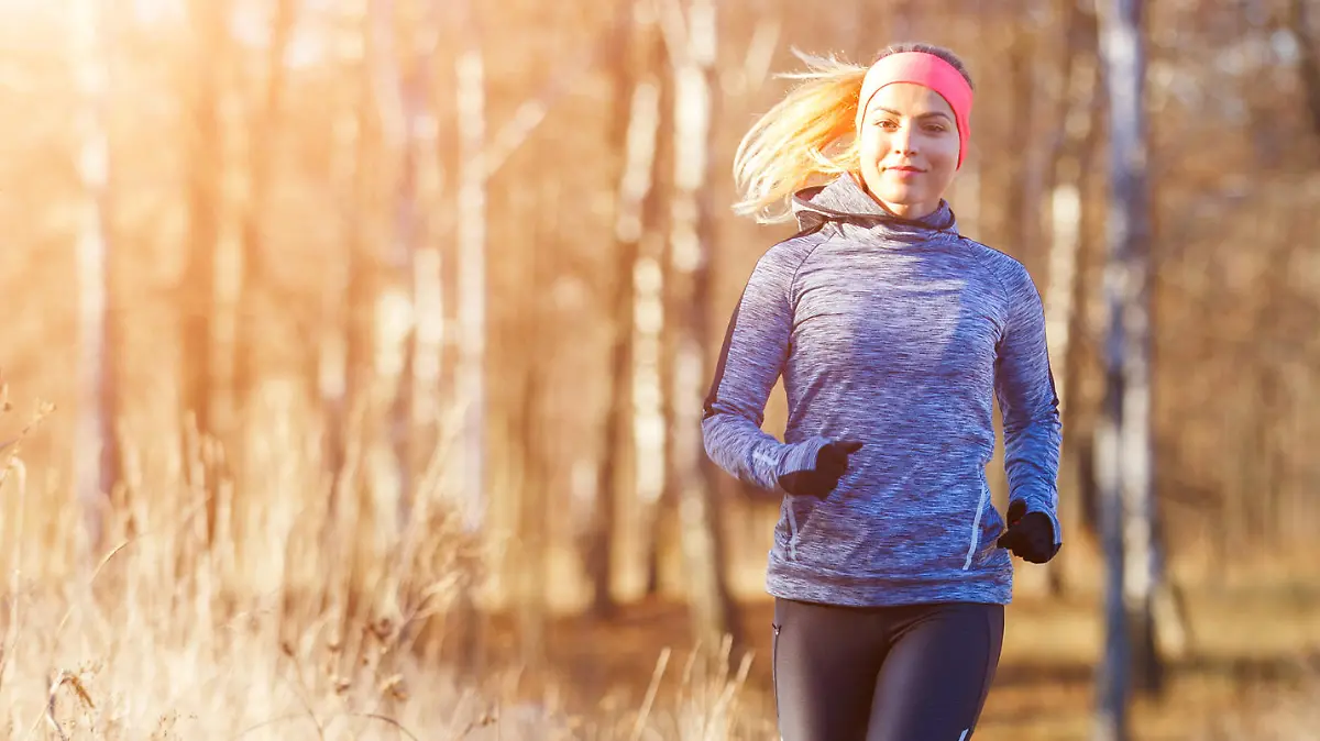 Young slim girl running in the park in early winter. Attractive woman jogging on snowy trail
