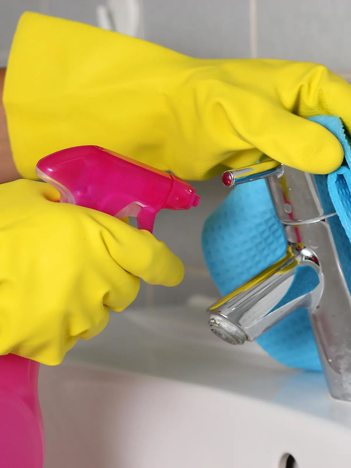Frauenhände mit Gummihandschuhen putzen ein Waschbecken
