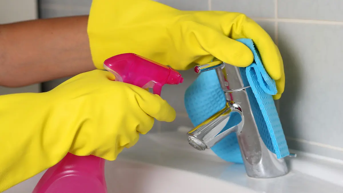 Frauenhände mit Gummihandschuhen putzen ein Waschbecken