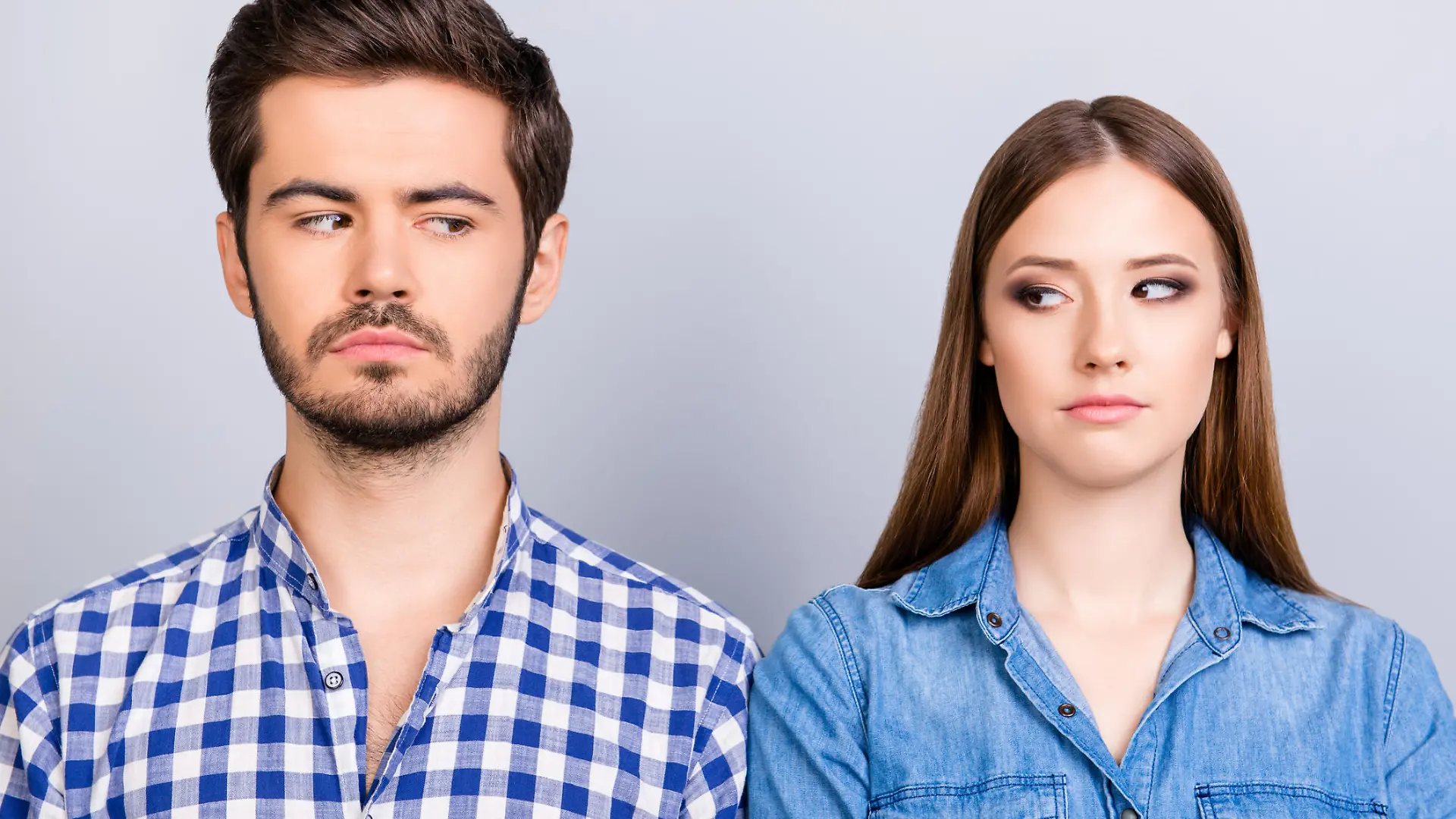 Mistrust and cheat problems. Annoyed couple is ignoring each other, but spy each other secretly, they stand on pure background in casual shirts