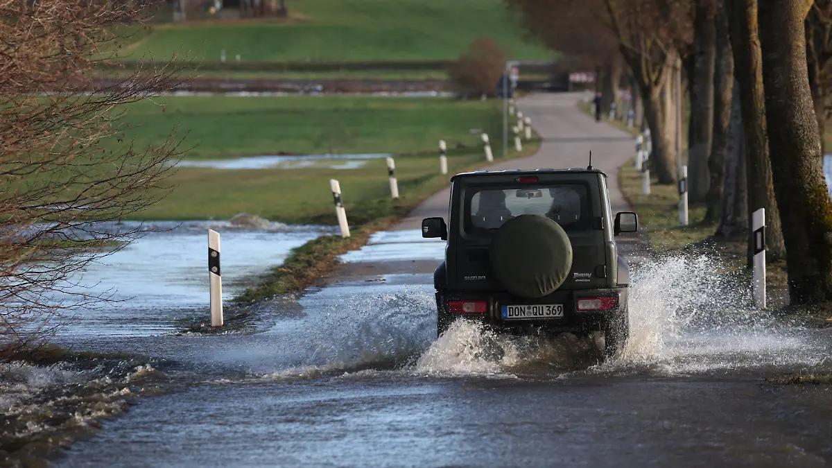 10.12.2023, Bayern, Gessertshausen: Ein Auto fährt auf einer vom Hochwasser der Schmutter überfluteten Straße. Foto: Karl-Josef Hildenbrand/dpa +++ dpa-Bildfunk +++
