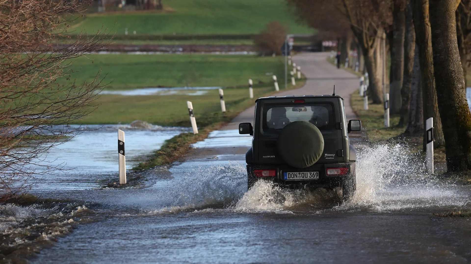 10.12.2023, Bayern, Gessertshausen: Ein Auto fährt auf einer vom Hochwasser der Schmutter überfluteten Straße. Foto: Karl-Josef Hildenbrand/dpa +++ dpa-Bildfunk +++