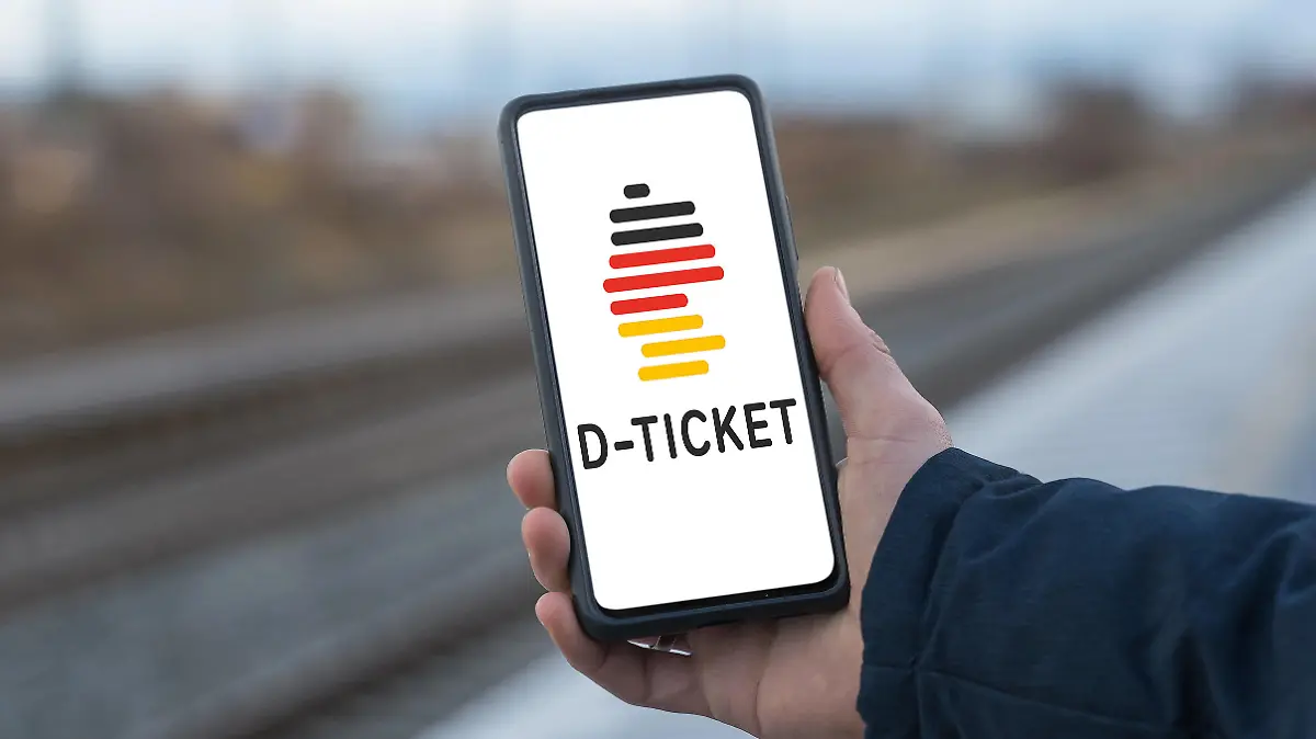 Augsburg, Bavaria, Germany - 28 April 2023: A man stands at the train station holding a smartphone with the D-Ticket Deutschlandticket app. The Deutschland Ticket also called 49 Euro Ticket is the successor of the 9 Euro Ticket FOTOMONTAGE *** Ein Mann steht am Bahnhof und hält ein Smartphone mit der D-Ticket Deutschlandticket App in der Hand. Das Deutschland Ticket auch 49 Euro Ticket genannt ist der Nachfolger des 9 Euro Tickets FOTOMONTAGE