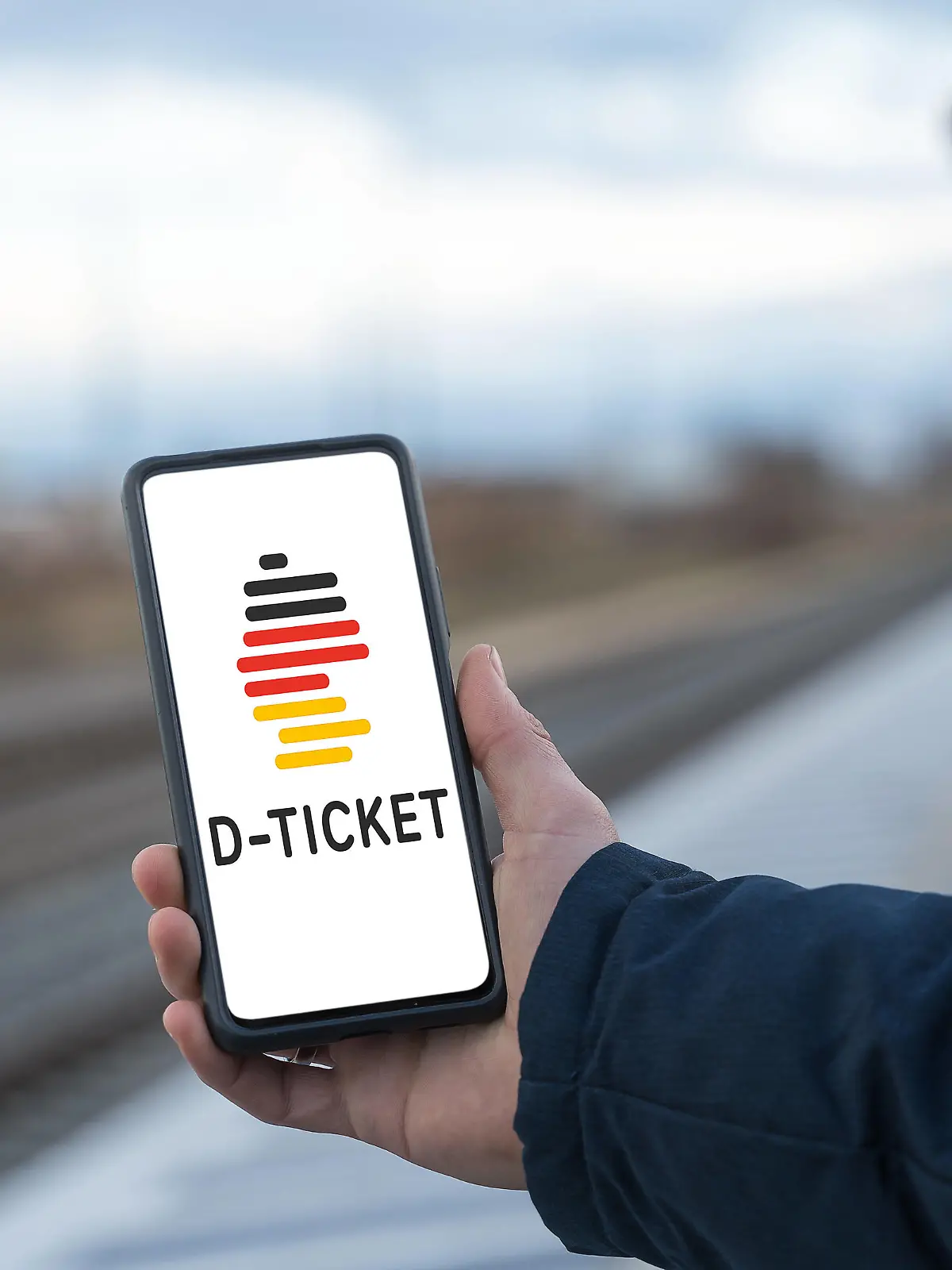 Augsburg, Bavaria, Germany - 28 April 2023: A man stands at the train station holding a smartphone with the D-Ticket Deutschlandticket app. The Deutschland Ticket also called 49 Euro Ticket is the successor of the 9 Euro Ticket FOTOMONTAGE *** Ein Mann steht am Bahnhof und hält ein Smartphone mit der D-Ticket Deutschlandticket App in der Hand. Das Deutschland Ticket auch 49 Euro Ticket genannt ist der Nachfolger des 9 Euro Tickets FOTOMONTAGE