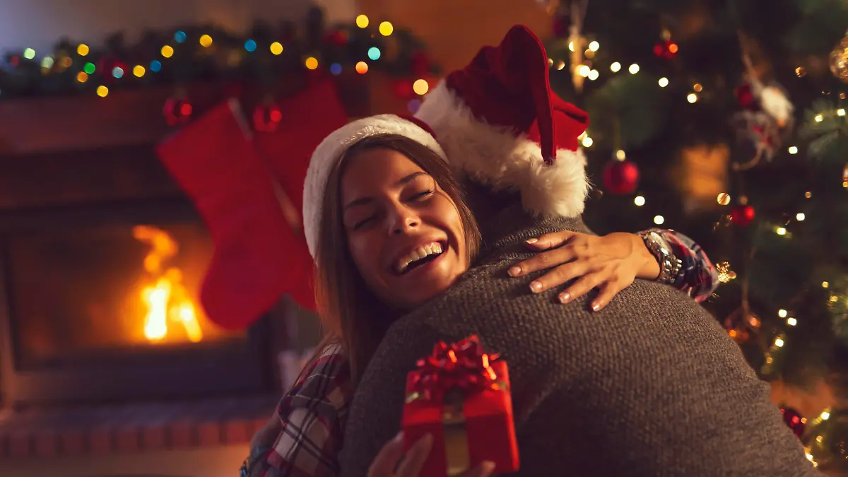 Young couple in love sitting by the fireplace and nicely decorated Christmas tree, exchanging Christmas presents