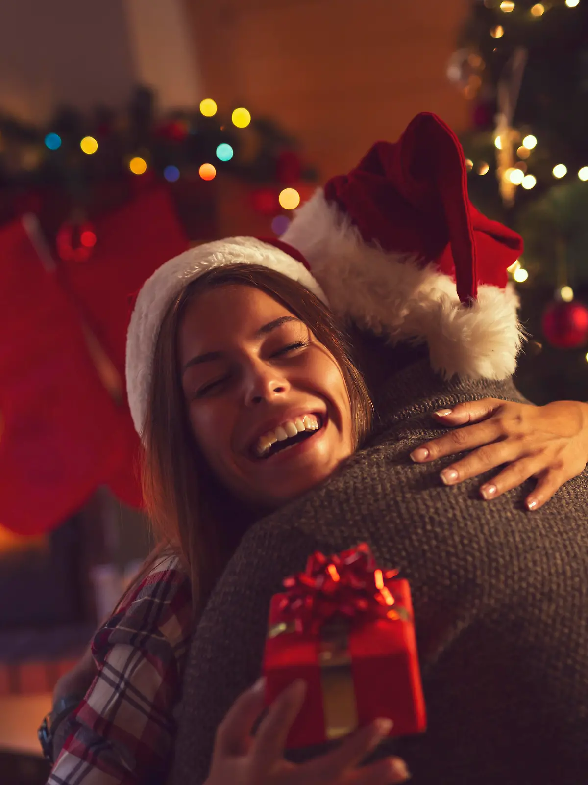 Young couple in love sitting by the fireplace and nicely decorated Christmas tree, exchanging Christmas presents