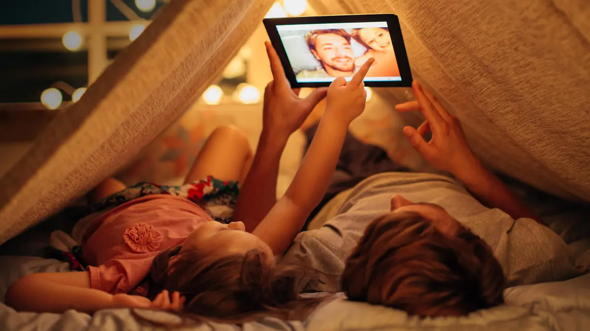Father and daughter enjoying at home. Lying on bed at night in do it yourself tent and using digital tablet together. Taking selfies and watching photos.