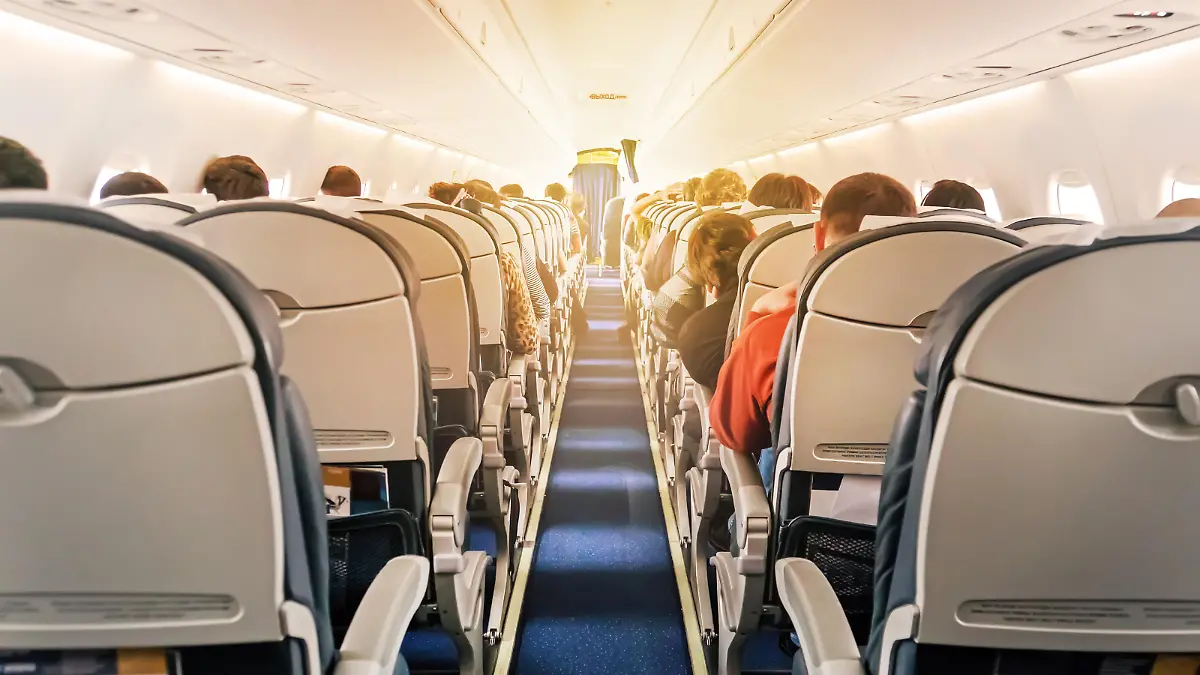 Eine kommerzielle Flugzeugkabine mit Sitzreihen, den Gang hinunter fotografiert, an einem frühen Morgen, wo das Licht durch die Flugzeugfenster fällt.