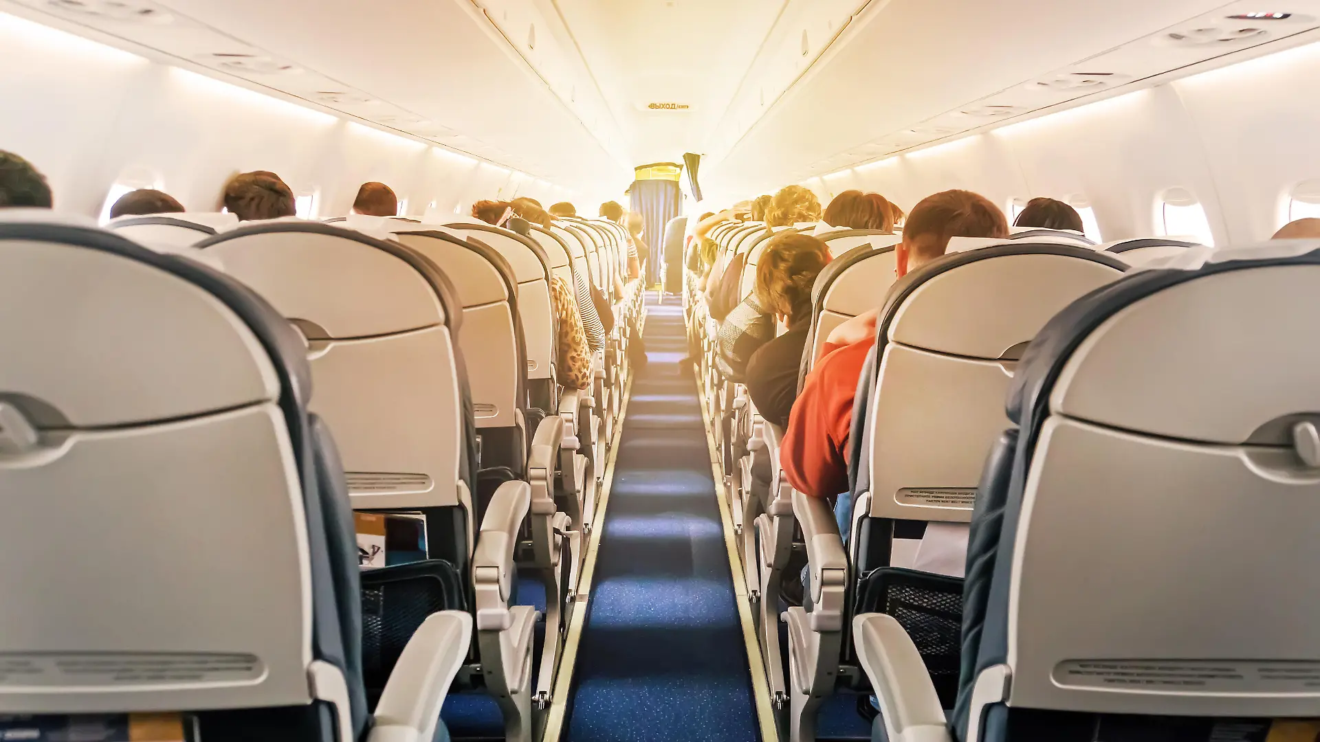 Eine kommerzielle Flugzeugkabine mit Sitzreihen, den Gang hinunter fotografiert, an einem frühen Morgen, wo das Licht durch die Flugzeugfenster fällt.