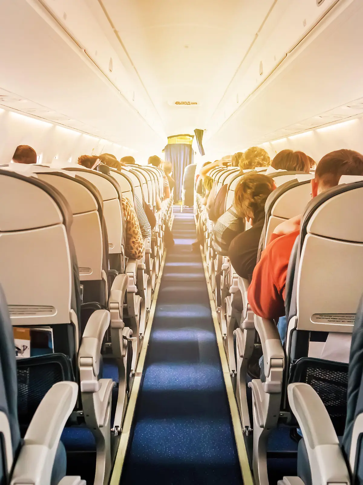 Eine kommerzielle Flugzeugkabine mit Sitzreihen, den Gang hinunter fotografiert, an einem frühen Morgen, wo das Licht durch die Flugzeugfenster fällt.