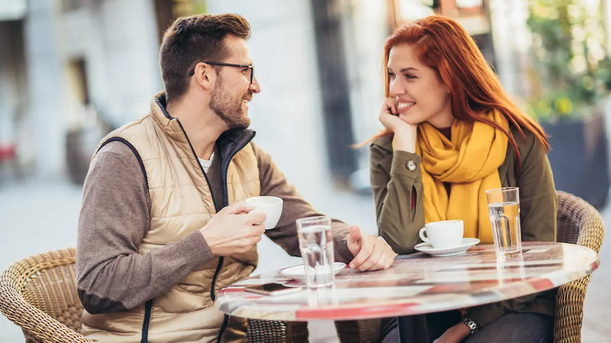Attractive young couple in love sitting at the cafe table outdoors, drinking coffee