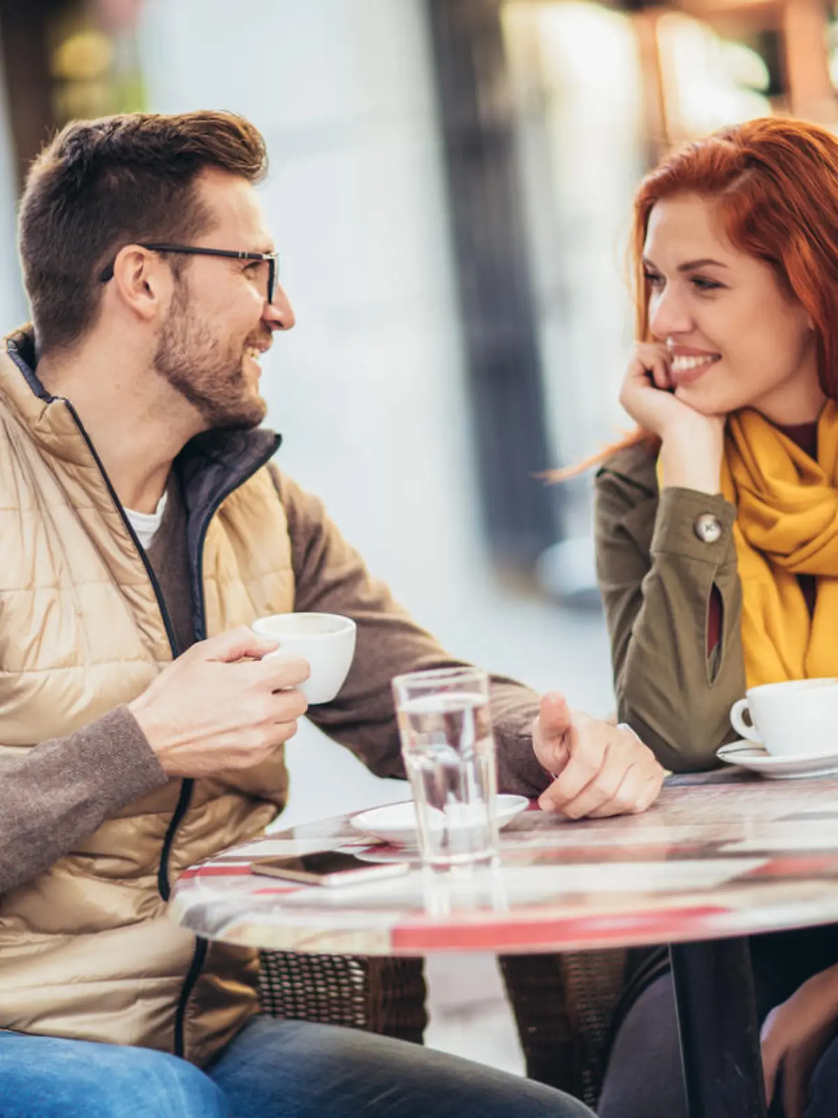 Attractive young couple in love sitting at the cafe table outdoors, drinking coffee