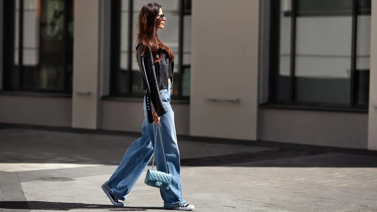 Frau in Baggy-Pants und blauer Tasche geht auf dem Gehweg.