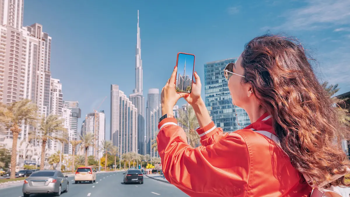 Tourist happy girl taking photos for her travel blog, in Dubai downtown district against background of the Burj Khalifa highest skyscraper