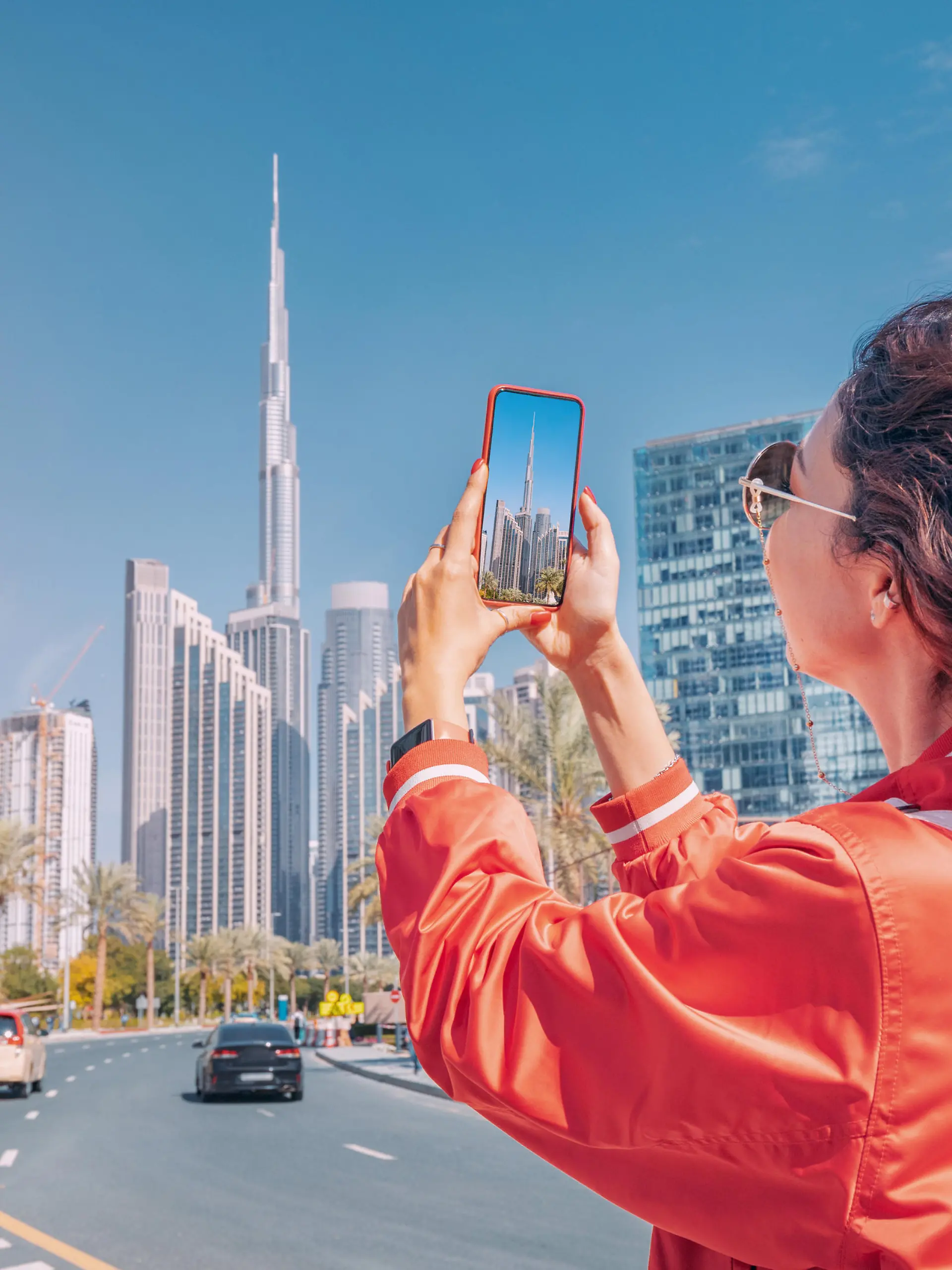 Tourist happy girl taking photos for her travel blog, in Dubai downtown district against background of the Burj Khalifa highest skyscraper