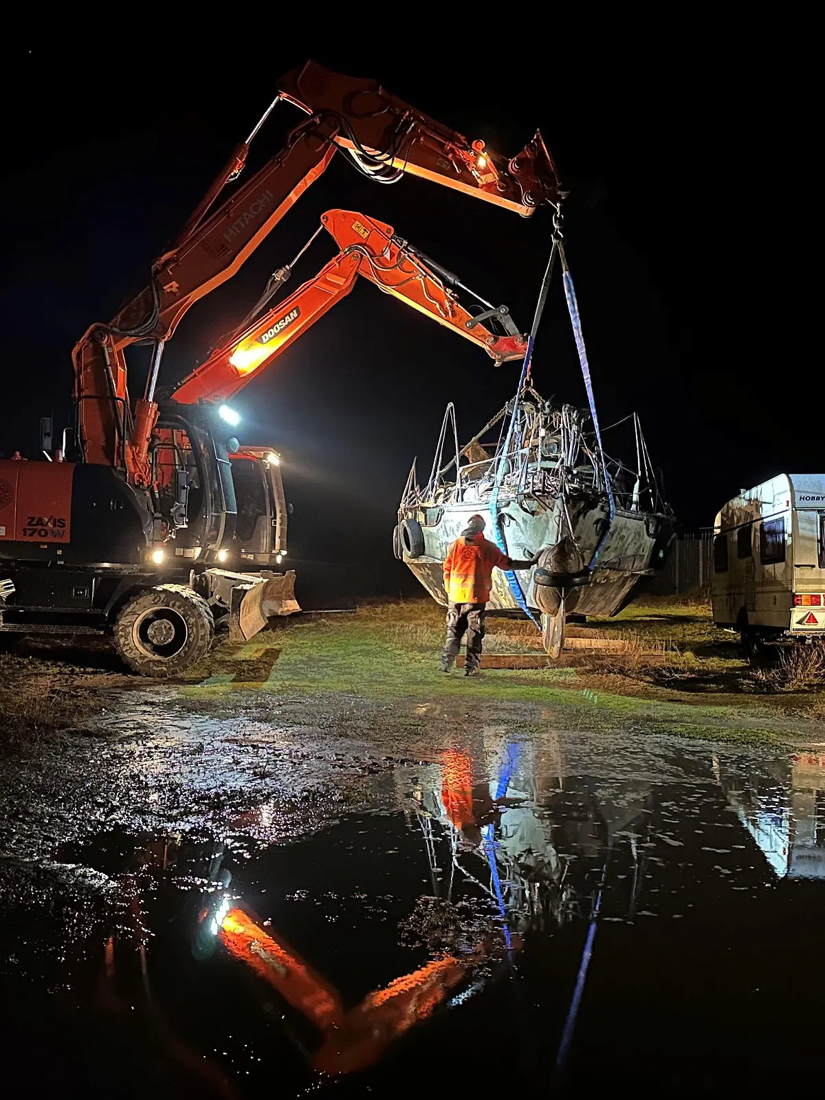 15.12.2023, Niedersachsen, Norderney: Zwei Bagger heben das im Hafen der Insel Norderney abgestellte und Anfang November gestrandete Segelboot für einen geplanten Abtransport zum Festland an. Ein für den Freitagmorgen geplanter Abtransport ans Festland mit einem Tieflader und einem Frachtschiff kam allerdings nicht zustande. (zu dpa: "Auf Norderney gestrandetes Segelboot kommt nicht von Insel los") Foto: Volker Bartels/dpa +++ dpa-Bildfunk +++