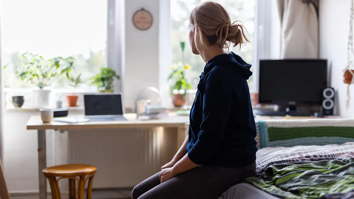 ARCHIV - 13.08.2023, Niedersachsen, Hannover: ILLUSTRATION - Eine Studentin sitzt auf dem Bett in ihrem WG-Zimmer und schaut aus dem Fenster (gestellte Szene). (Zu dpa "WHO will gegen Einsamkeit als Gesundheitsrisiko vorgehen") Foto: Michael Matthey/dpa - ACHTUNG: Nur zur redaktionellen Verwendung und nur mit vollständiger Nennung des vorstehenden Credits +++ dpa-Bildfunk +++