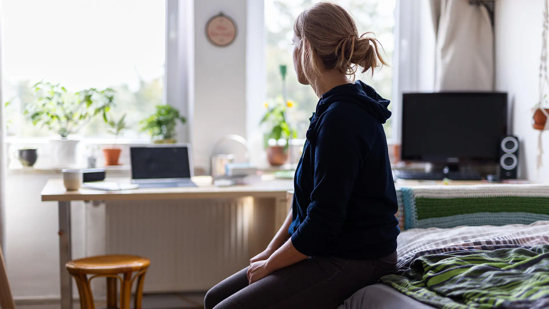ARCHIV - 13.08.2023, Niedersachsen, Hannover: ILLUSTRATION - Eine Studentin sitzt auf dem Bett in ihrem WG-Zimmer und schaut aus dem Fenster (gestellte Szene). (Zu dpa "WHO will gegen Einsamkeit als Gesundheitsrisiko vorgehen") Foto: Michael Matthey/dpa - ACHTUNG: Nur zur redaktionellen Verwendung und nur mit vollständiger Nennung des vorstehenden Credits +++ dpa-Bildfunk +++