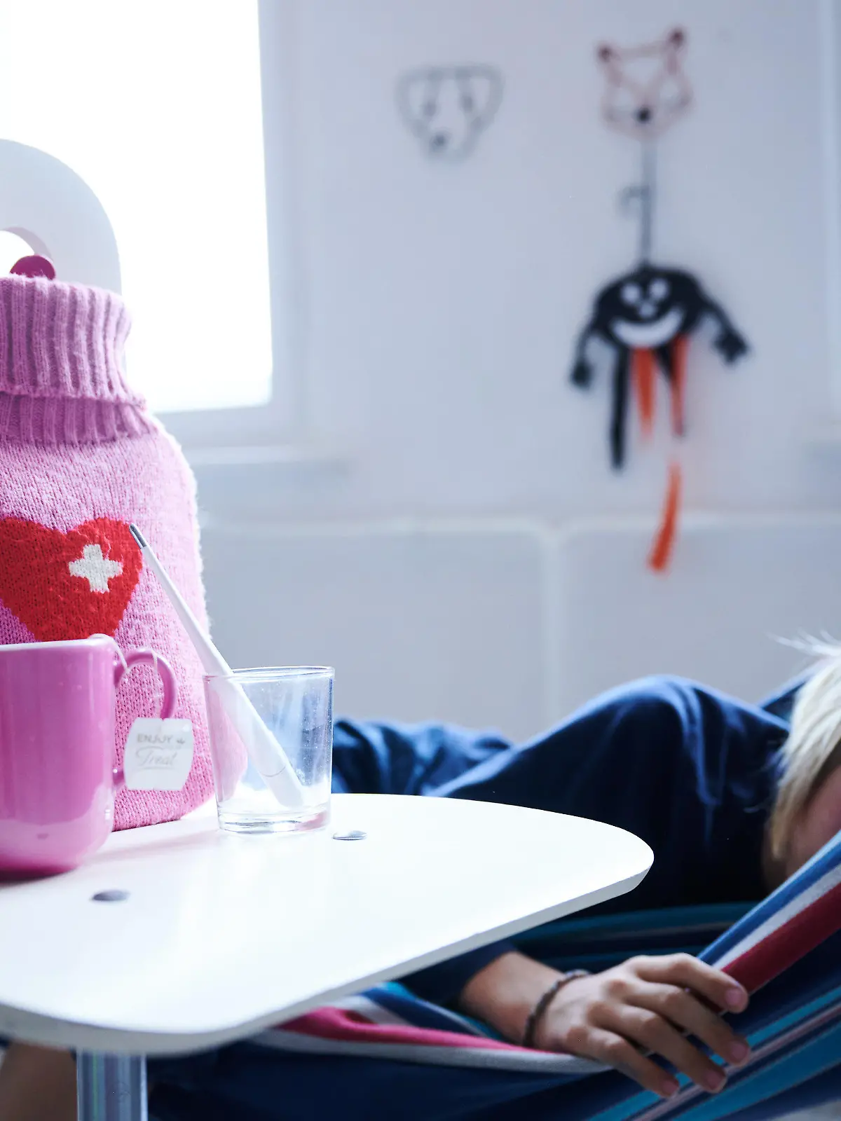 ILLUSTRATION - 11.09.2021, Berlin: Fieberthermometer, Hustensaft, Wärmflasche und eine Tasse Tee stehen auf einem Stuhl, während ein Kind im Hintergrund in einer Hängematte liegt (gestellte Szene). Bundesgesundheitsminister Karl Lauterbach (SPD) möchte die telefonische Krankschreibung auch für Eltern erkrankter Kinder einführen. Vor kurzem erst war die in früheren Corona-Wellen praktizierte telefonische Krankschreibung für selbst erkrankte Erwachsene wieder eingeführt worden.(zu dpa «Lauterbach dringt auf telefonische Kinderkrankmeldung für Eltern») Foto: Annette Riedl/dpa +++ dpa-Bildfunk +++