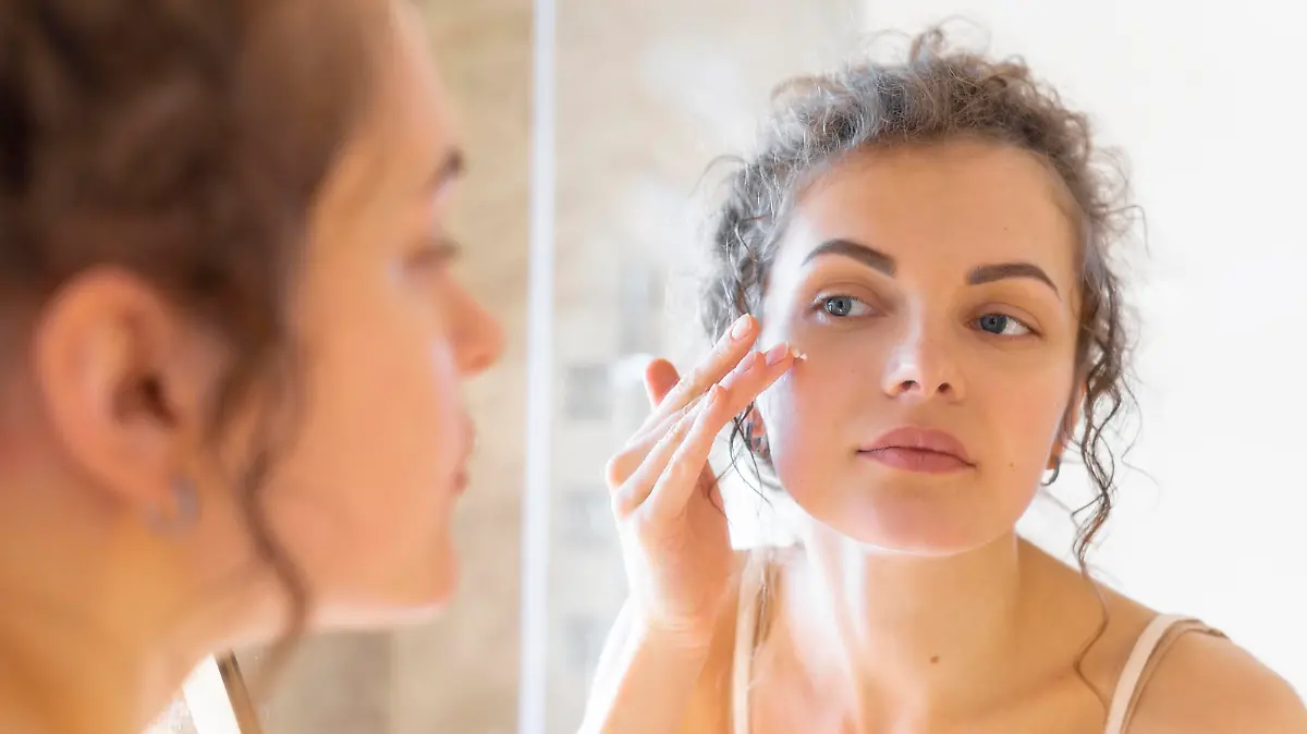 woman looking mirror applying cream face || Modellfreigabe vorhanden