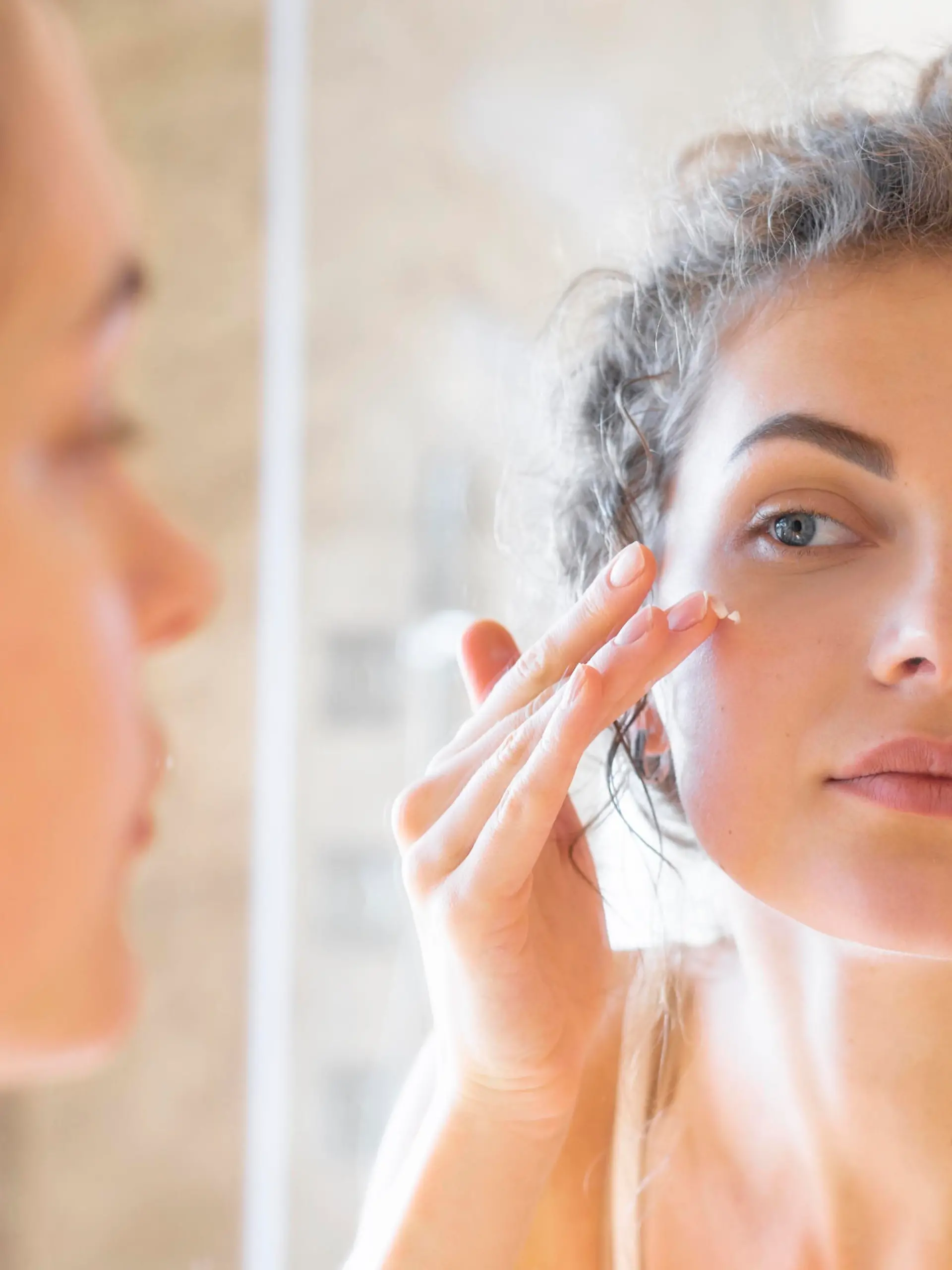 woman looking mirror applying cream face || Modellfreigabe vorhanden