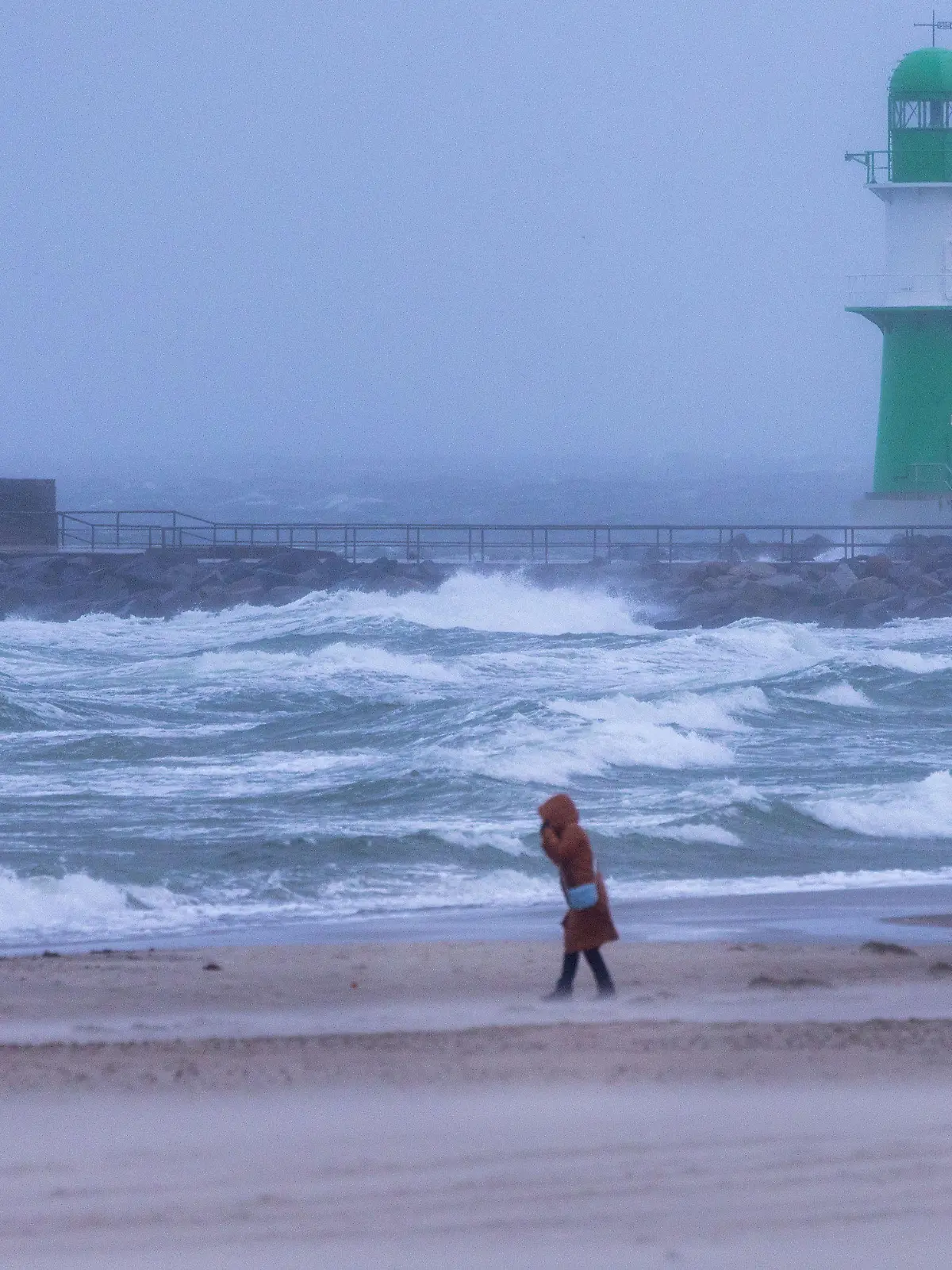 16.11.2023, Mecklenburg-Vorpommern, Rostock: Eine Frau geht bei Sturm und Regen über den Strand an der Ostseeküste in Warnemünde. In Mecklenburg-Vorpommern zeigt sich das Herbstwetter mit Böen, vielen Wolken und kräftigem Regen von seiner unfreundlichen Seite. Nach Angaben des Deutschen Wetterdienstes (DWD) kann es an der Küste zu Sturmböen mit bis zu 80 Kilometern pro Stunde kommen. Foto: Jens Büttner/dpa +++ dpa-Bildfunk +++