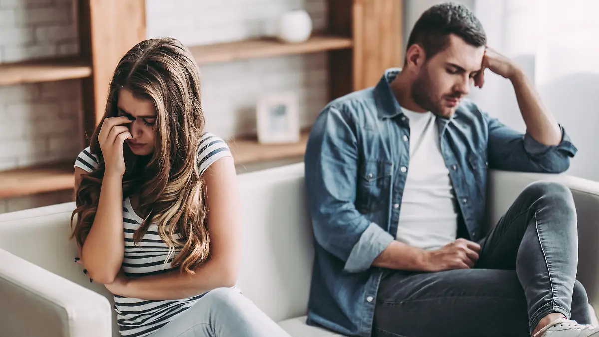 Upset couple at home. Handsome man and beautiful young woman are having quarrel. Sitting on sofa together. Family problems.