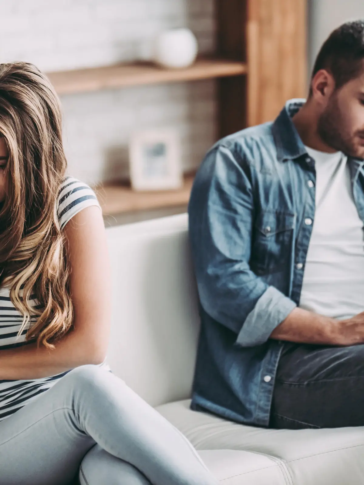 Upset couple at home. Handsome man and beautiful young woman are having quarrel. Sitting on sofa together. Family problems.