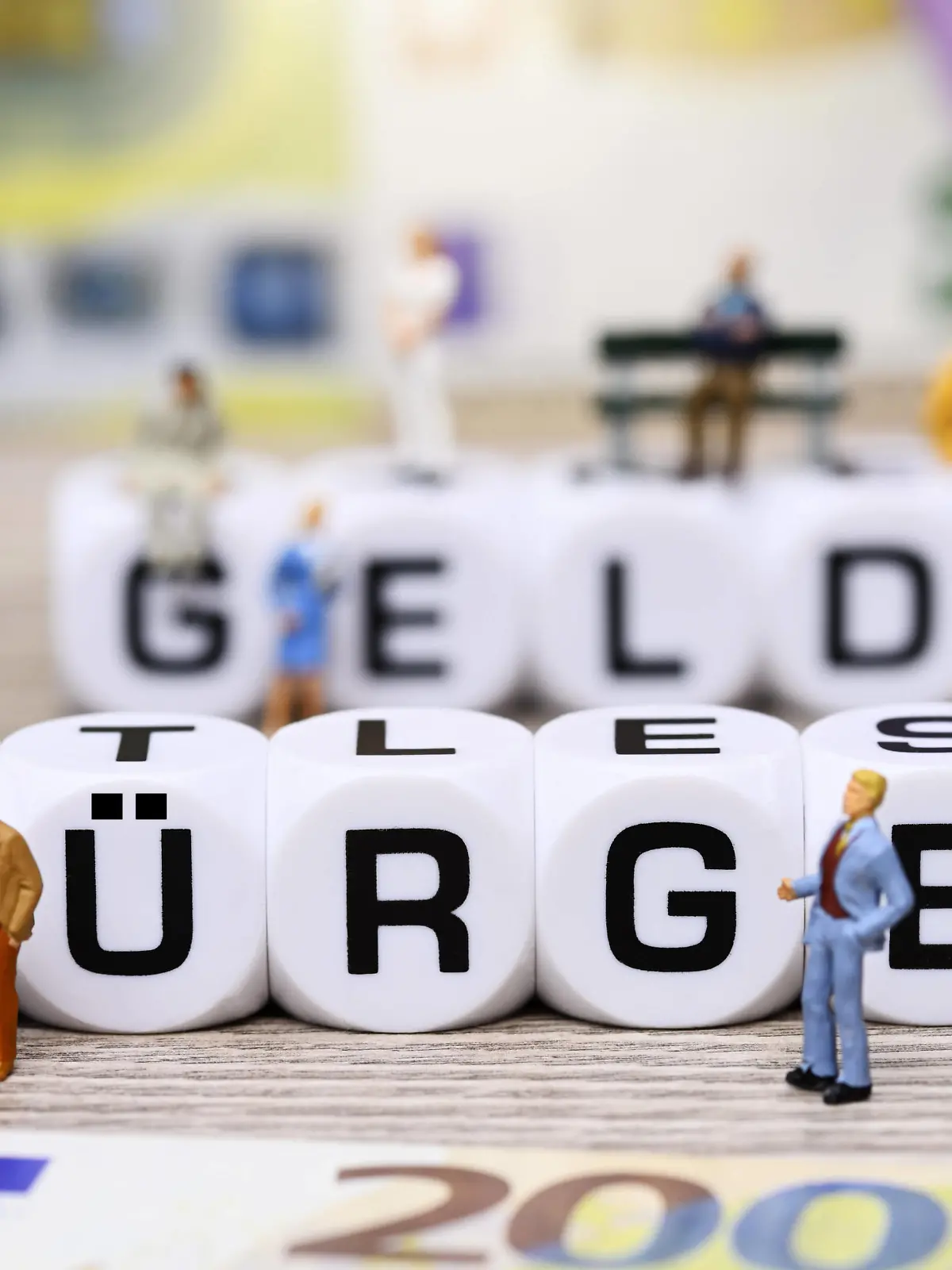 Würfelbuchstaben formen den Schriftzug Bürgergeld umgeben von Miniaturfiguren *** Cube letters form the lettering Bürgergeld surrounded by miniature figures 
