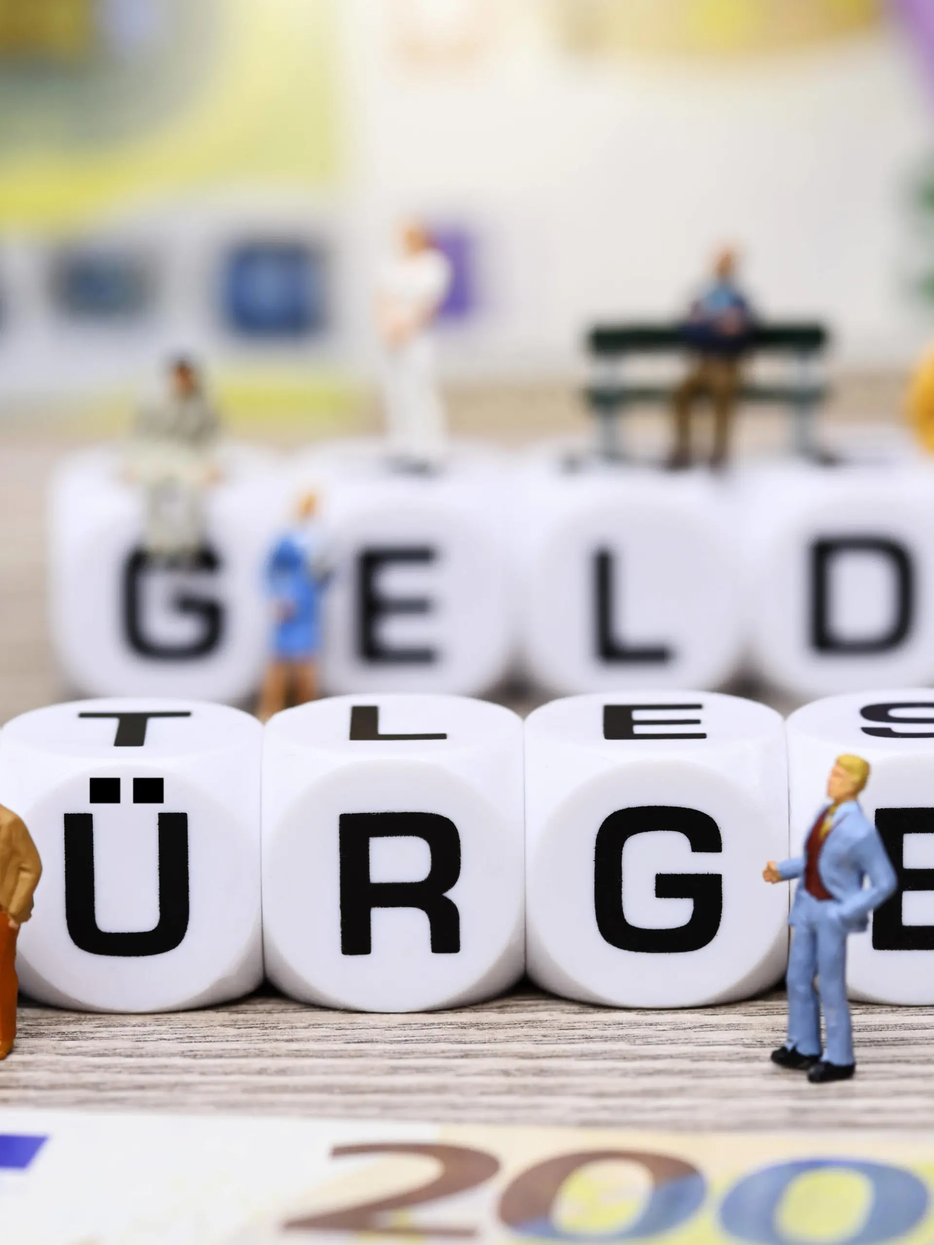 Würfelbuchstaben formen den Schriftzug Bürgergeld umgeben von Miniaturfiguren *** Cube letters form the lettering Bürgergeld surrounded by miniature figures 