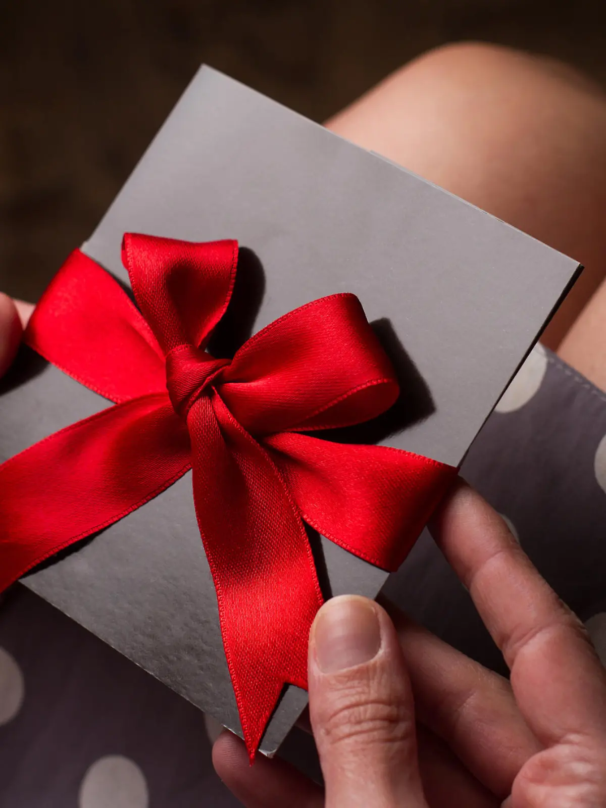 Close up of the hands of a woman with polka dress holding a black card with red ribbon above knees