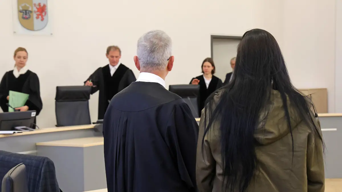 19.12.2023, Mecklenburg-Vorpommern, Rostock: Ullrich Knye, Verteidiger, und die Angeklagte im Prozess wegen Mordes durch Unterlassung stehen im Saal des Landgerichts während des Einzugs des Gerichts und warten auf die Urteilsverkündung. Laut Anklage soll die 24-Jährige ihren einjährigen Sohn nicht ausreichend mit Nahrung und Flüssigkeit versorgt und keinen Arzt konsultiert haben, als er krank wurde. Stattdessen habe sie das Kind in ihrer Wohnung allein gelassen, um Zeit mit ihrem Freund zu verbringen. Der Junge starb im September 2021 infolge starken Durchfalls an einem Gerinnsel in den Lungenschlagadern. Foto: Bernd Wüstneck/dpa +++ dpa-Bildfunk +++