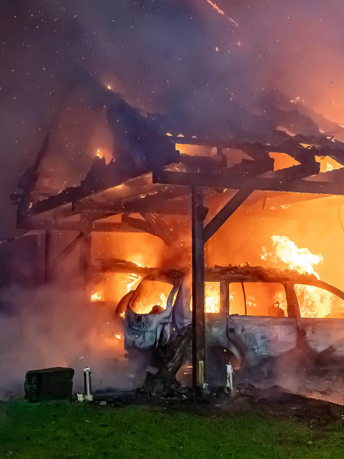 20.12.2023, Nordrhein-Westfalen, Wipperfürth: Feuerwehrleute bekämpfen einen Brand, während im Vordergrund ein Auto in einem Carport in Flammen steht. Bei dem Feuer in einer Wohnsiedlung sind in der Nacht zu Mittwoch, 20. Dezember, zwei Einfamilienhäuser zerstört worden, ausserdem eine Garage und ein Carport sowie insgesamt drei Autos. Von dem Carport aus schlugen die Flammen auf die Dachstühle der angrenzenden Wohnhäuser. Beide wurden durch den Brand unbewohnbar. Zwei Familien mit insgesamt sechs Kindern verlieren kurz vor Weihnachten ihr Heim. Bei den Löscharbeiten wurde ein Feuerwehrmann verletzt. Foto: Markus Klümper/dpa +++ dpa-Bildfunk +++