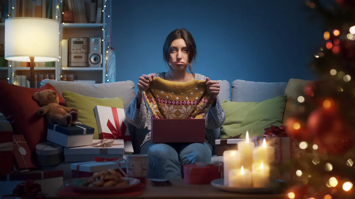 Sad disappointed woman opening Christmas gifts at home, she has received an ugly Christmas sweater