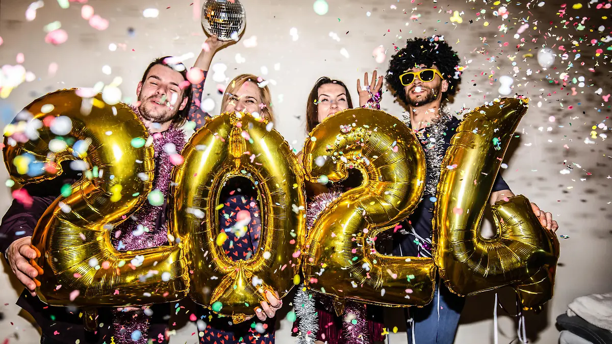 Four friends are celebrating the New Year 2024 with a party and big shiny foil balloons for 2024 and lots of falling confetti