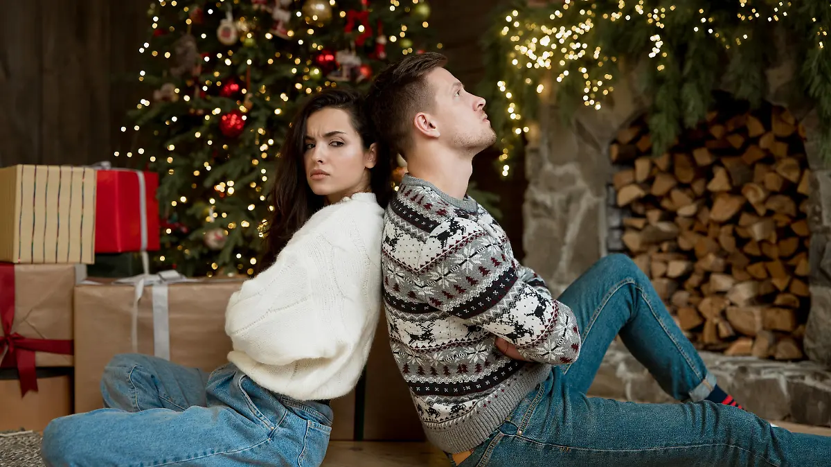 yound couple husband sitting with his back to his beautiful wife in room decorated for celebrating new year after having fight quarreling atmosphere.