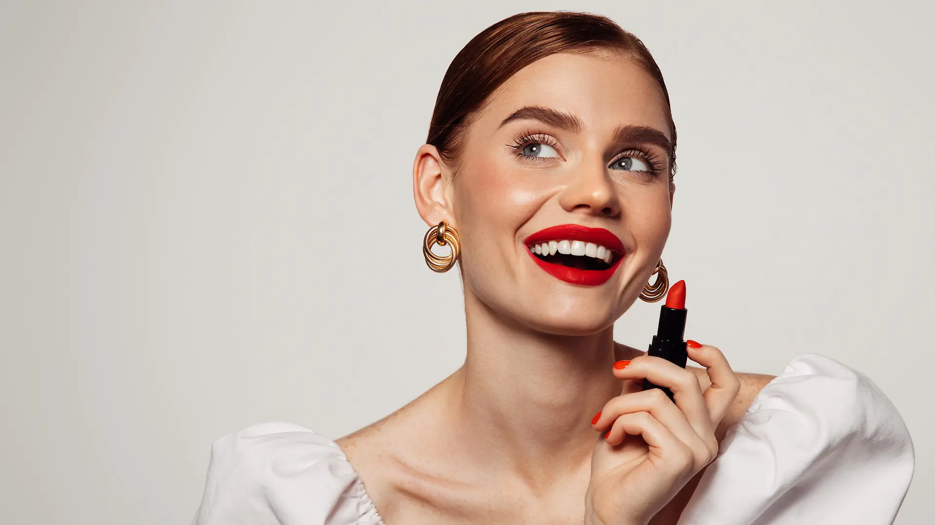 Beautiful emotional woman with bright make-up applying red lipstick