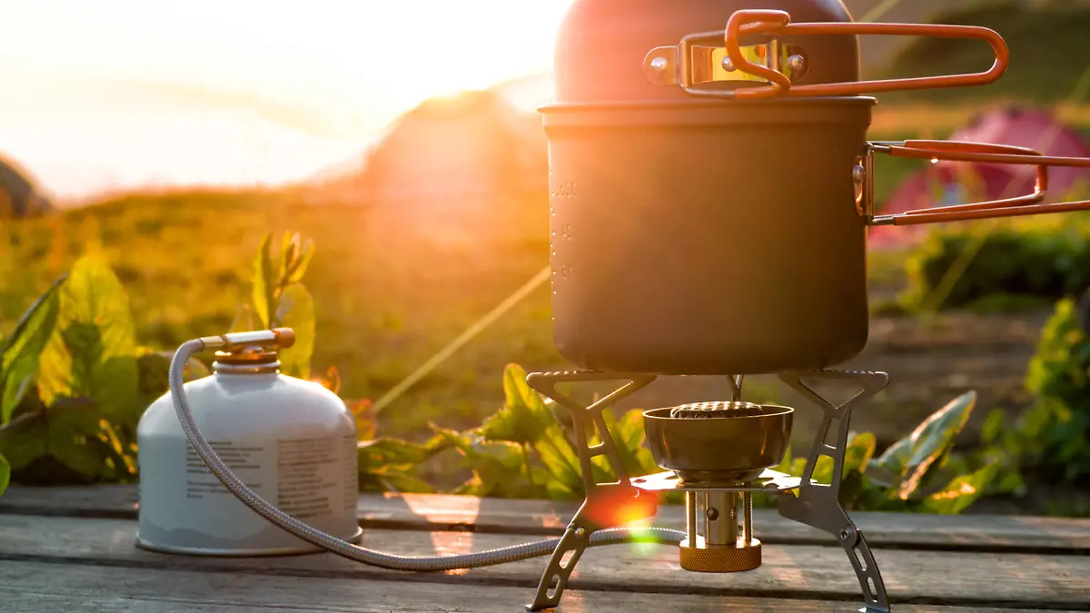 Cooking pot on camping gas stove and canister on wooden table at sunlight background. Travel equipment for hiking and backpacking at beautiful sunset